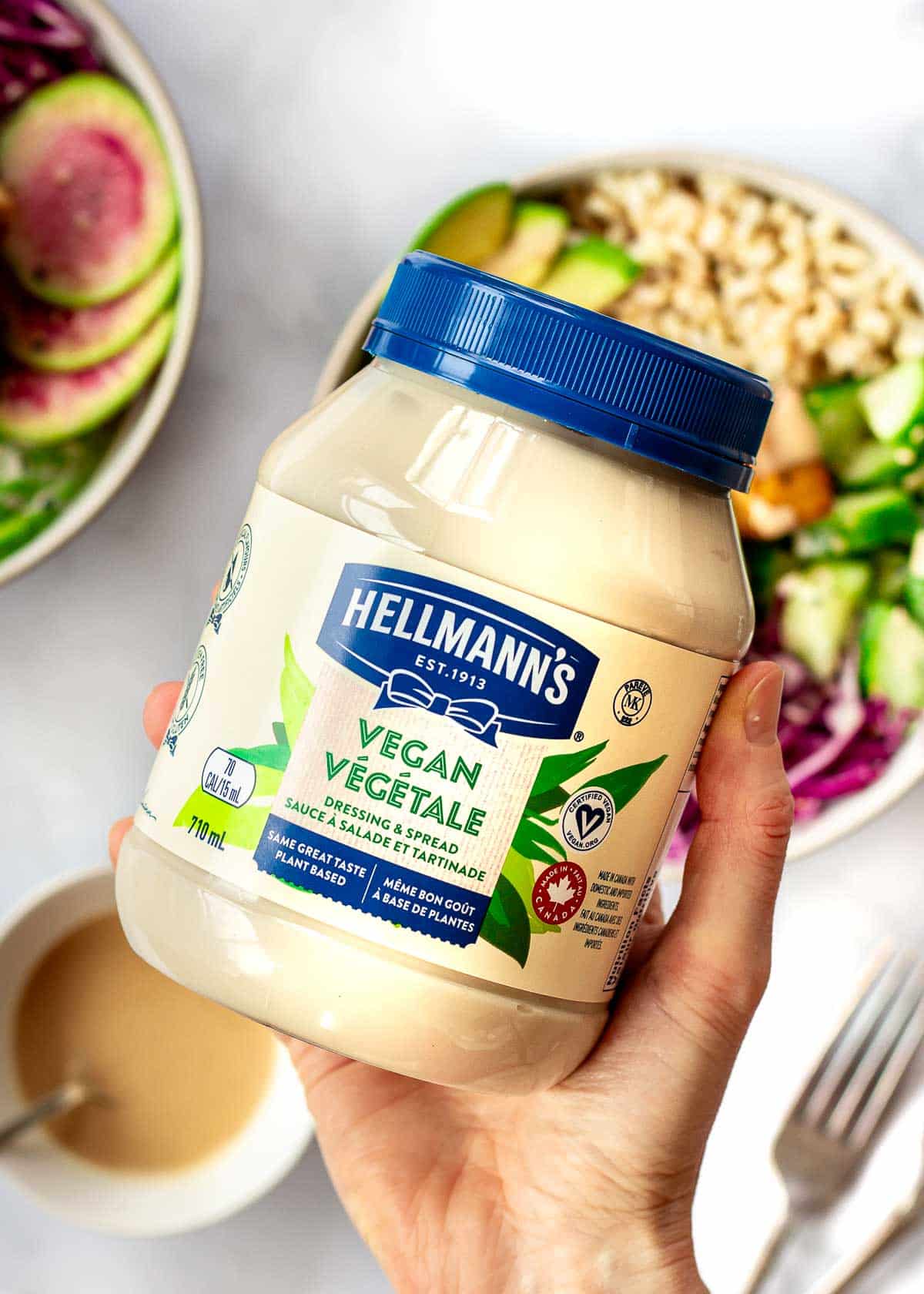 Woman's hand holding bottle of vegan mayonnaise in front of rice bowls.