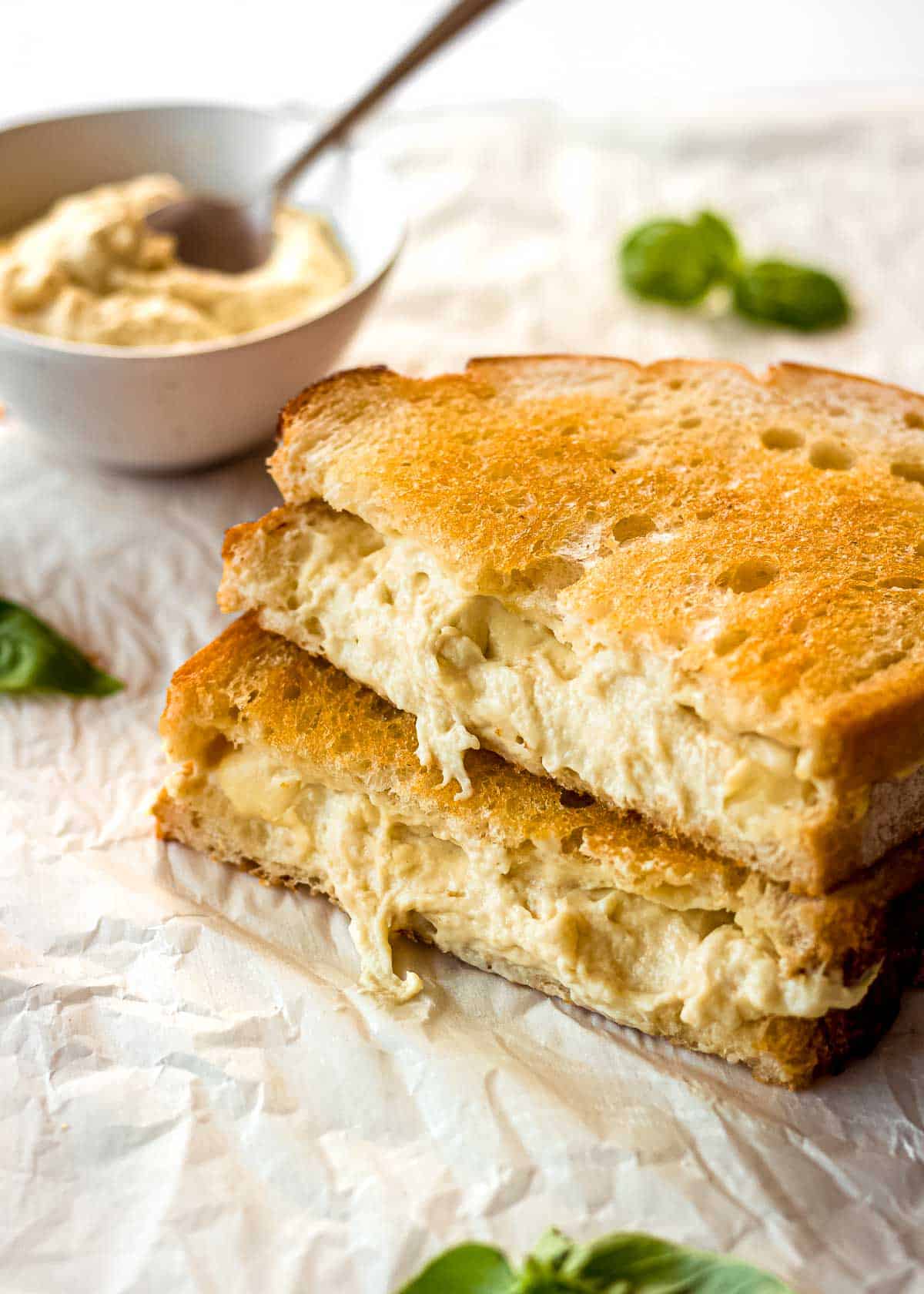 A grilled cheese sandwich made with cashew mozzarella, with a dish of the mozzarella in the background.