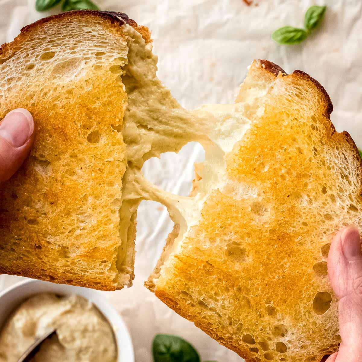 Hands pulling apart a grilled cheese sandwich filled with vegan mozzarella.