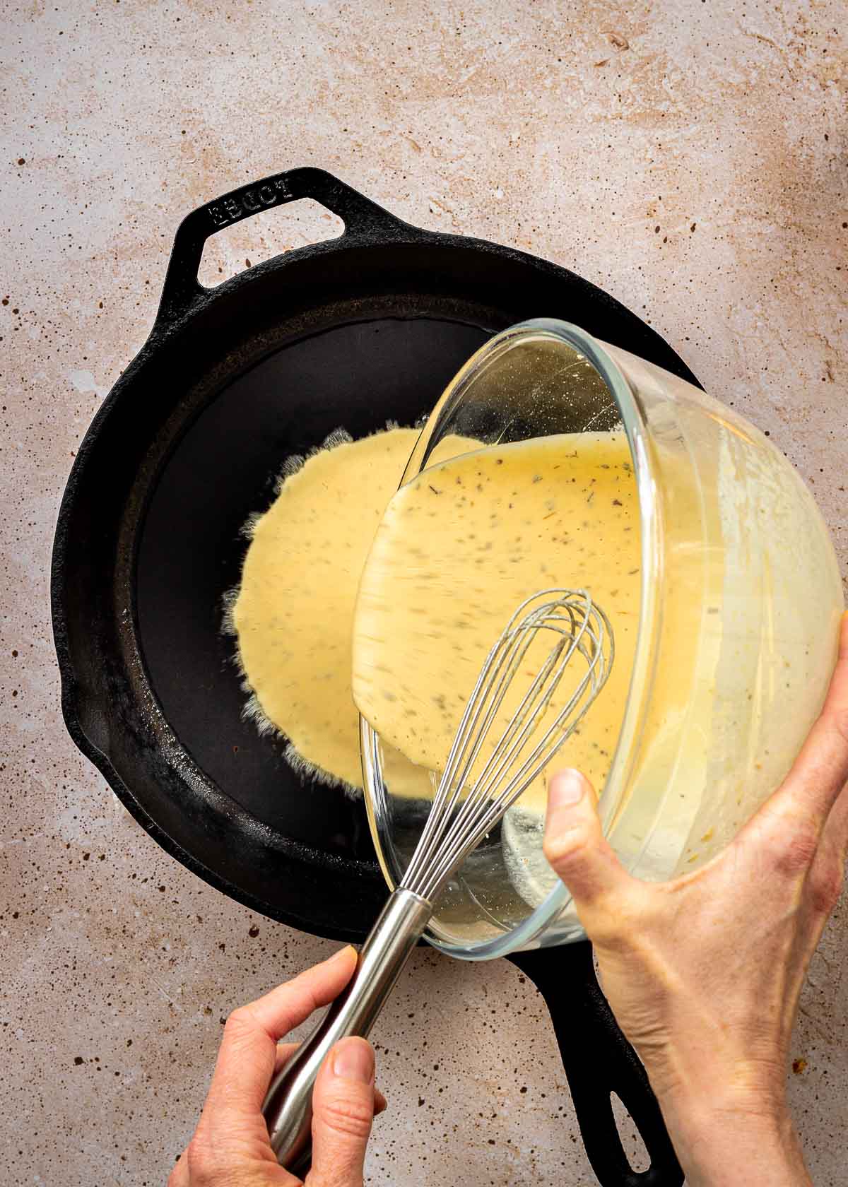 Chickpea pizza batter being poured into hot cast iron pan.