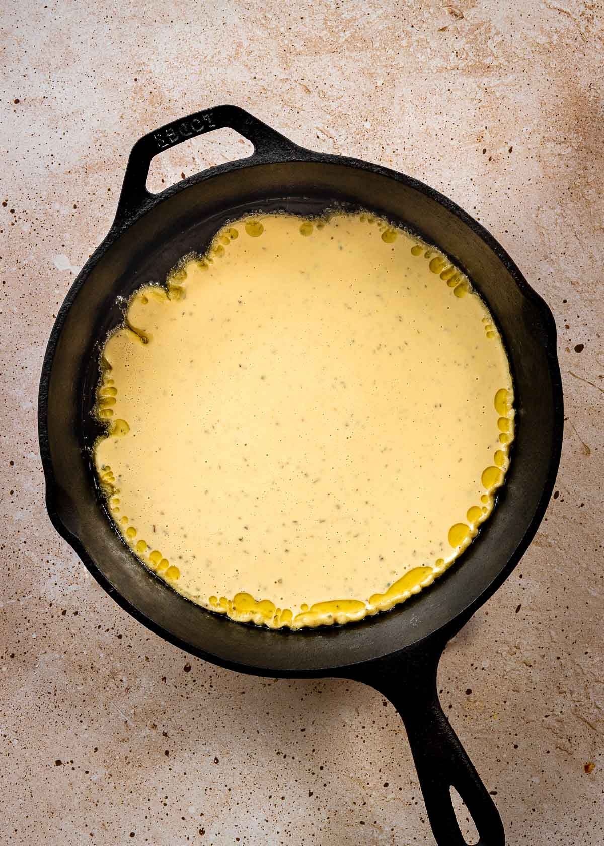Uncooked chickpea pizza batter in hot cast iron pan.