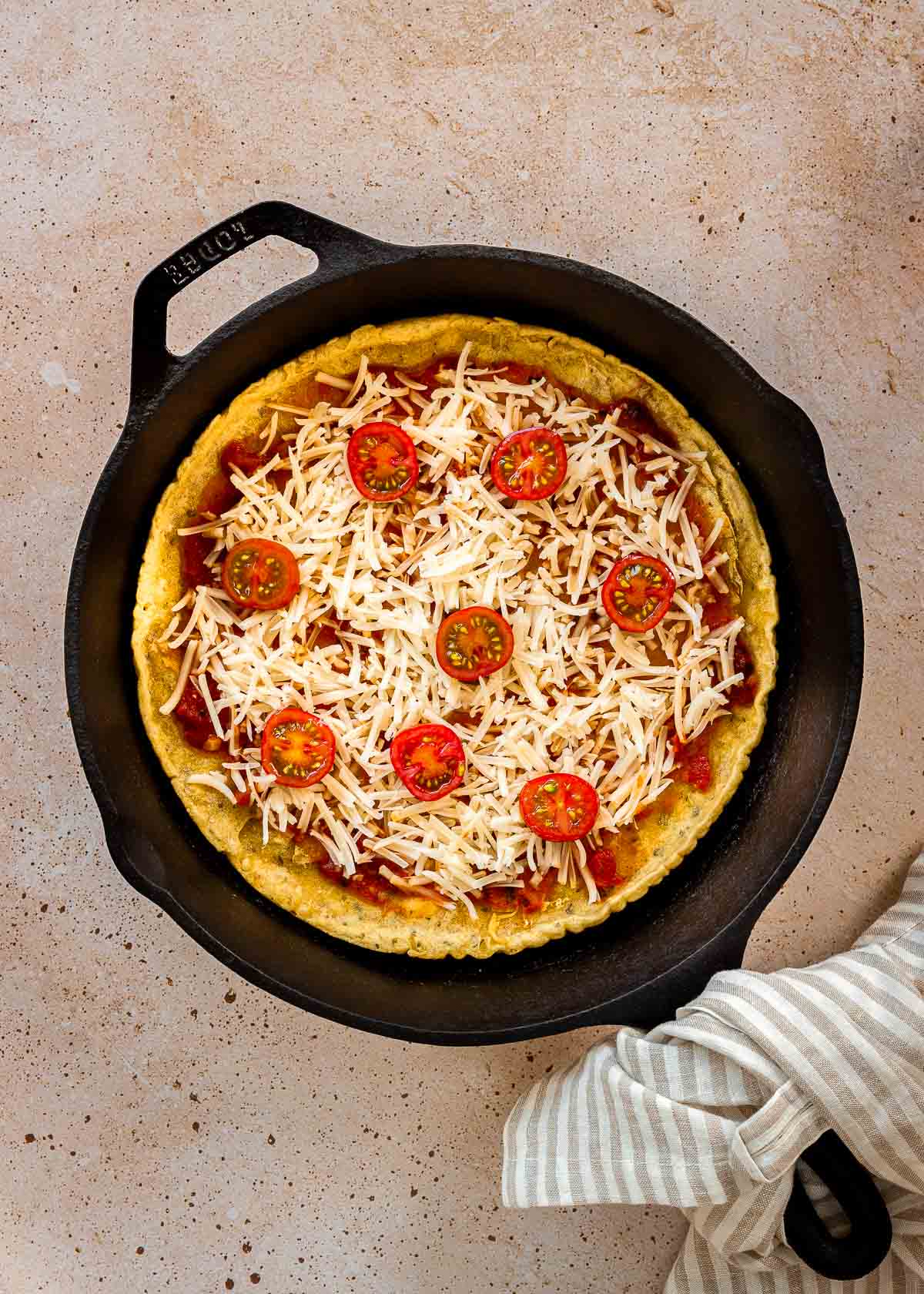 Chickpea pizza crust with uncooked toppings in cast iron pan.