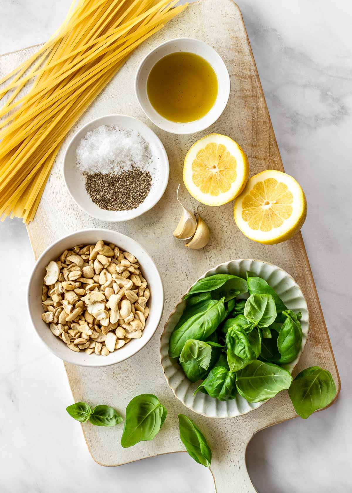 Ingredients on a chopping board for pasta al pesto - linguine, basil, lemon juice, garlic and oil etc.