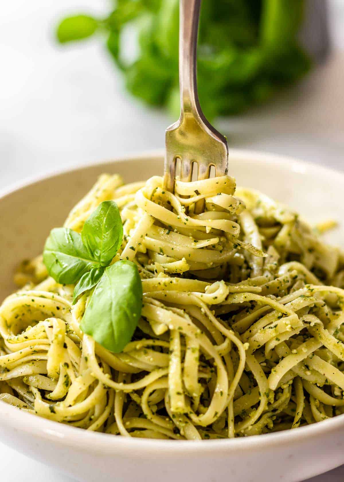 White bowl of pasta al pesto with basil and a fork being twisted in it.