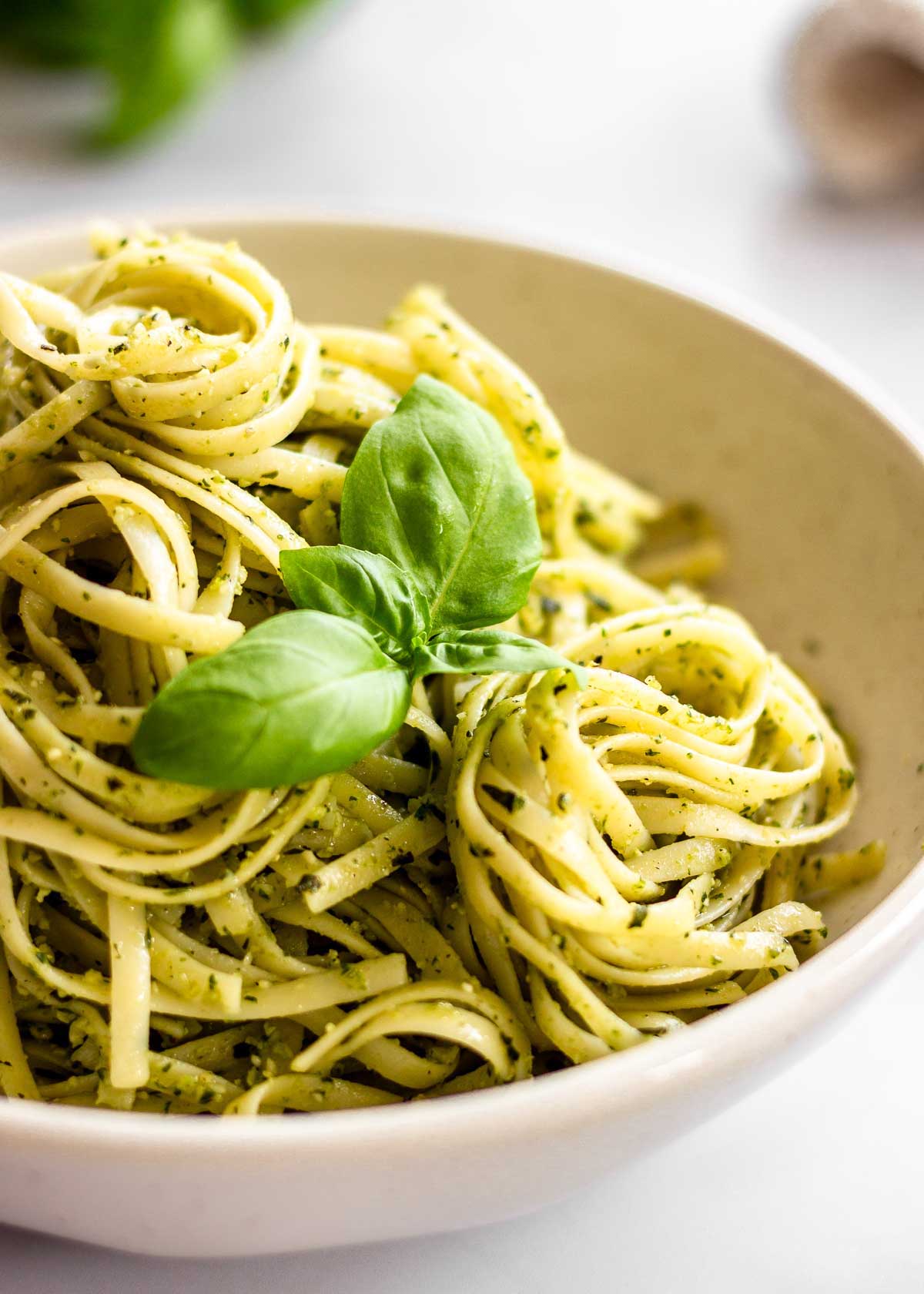 White bowl of pasta al pesto with basil leaves and on top.