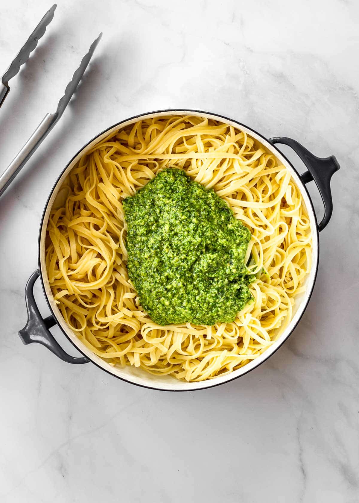 Large pot of cooked pasta with fresh basil pesto on top.