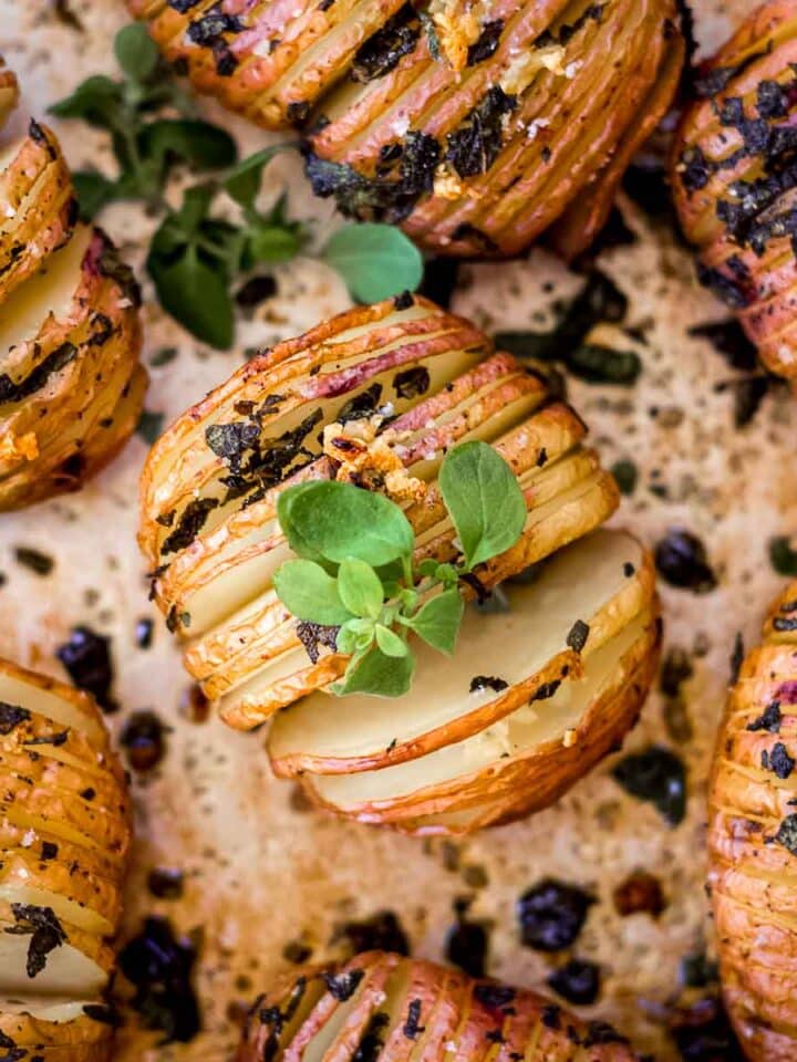 Garlic hasselback potatoes on a silver baking sheet, decorated with fresh herbs.