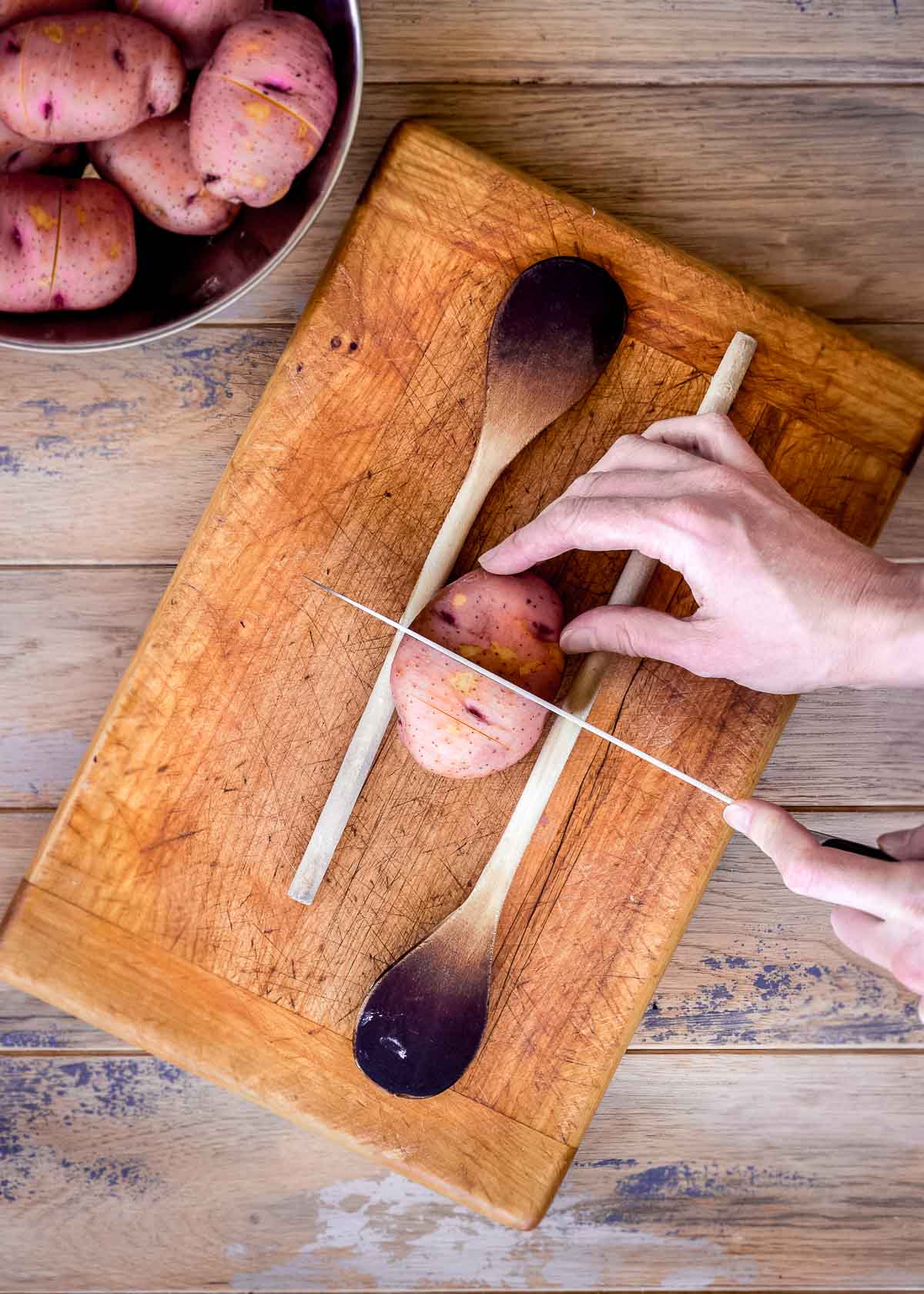 Τα χέρια μιας γυναίκας δείχνουν πώς να κόψετε μια πατάτα για πατάτες με κουκούτσι.