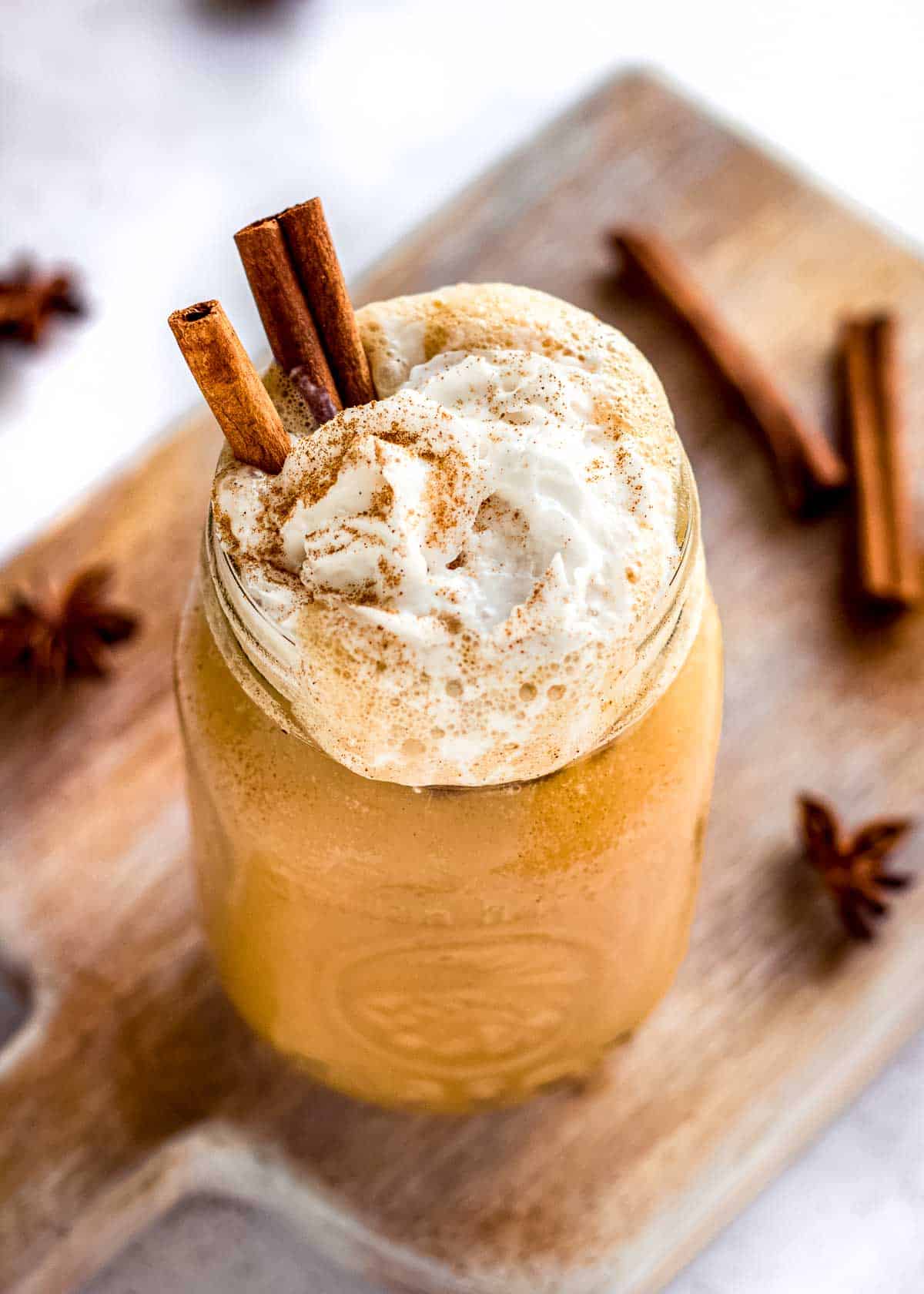 Iced pumpkin spice latte in a glass, topped with coconut whipped cream, cinnamon sticks and pumpkin spice. Cinnamon sticks and star anise are nearby.