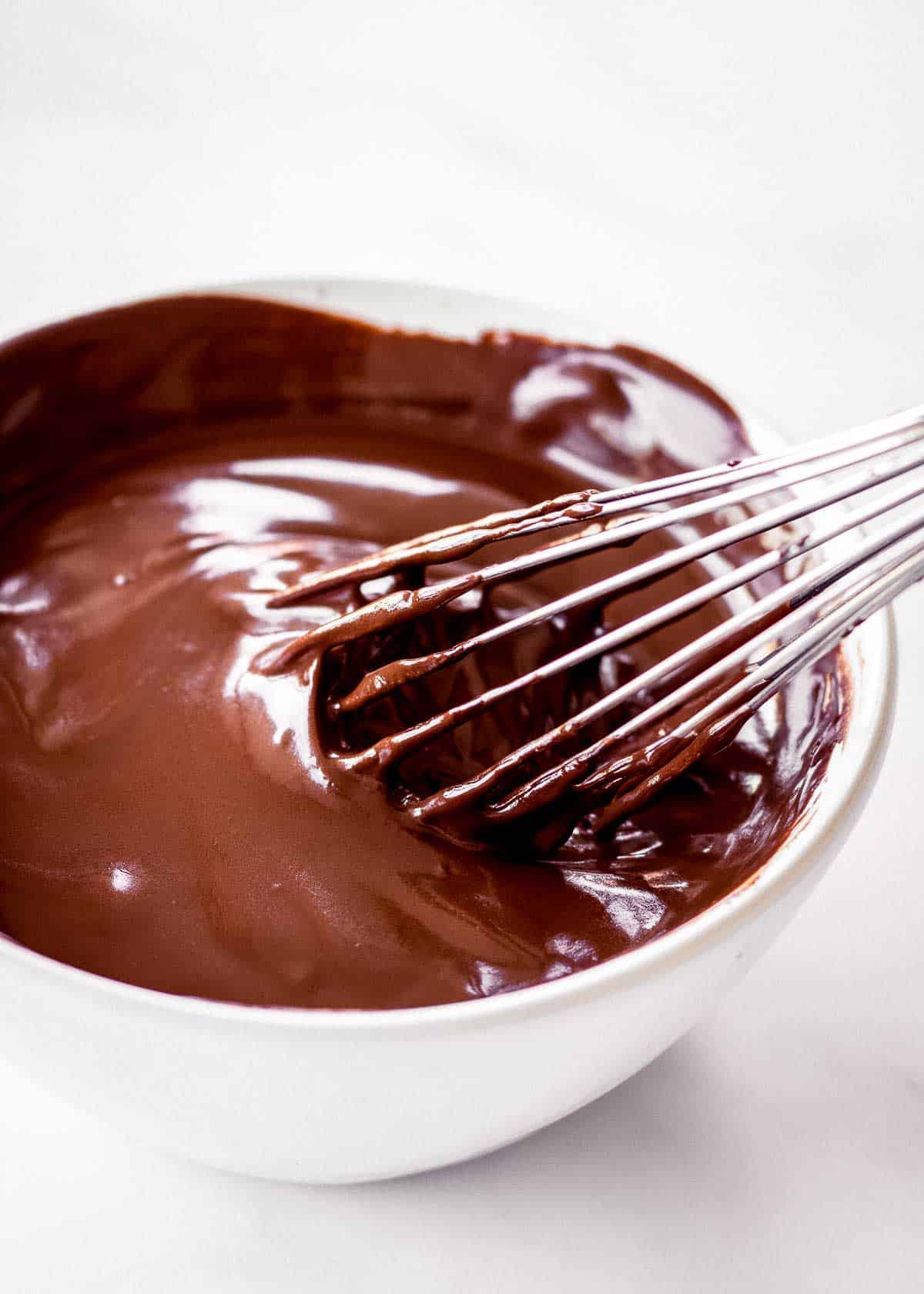 A metal whisk sits in a bowl of vegan chocolate ganache.