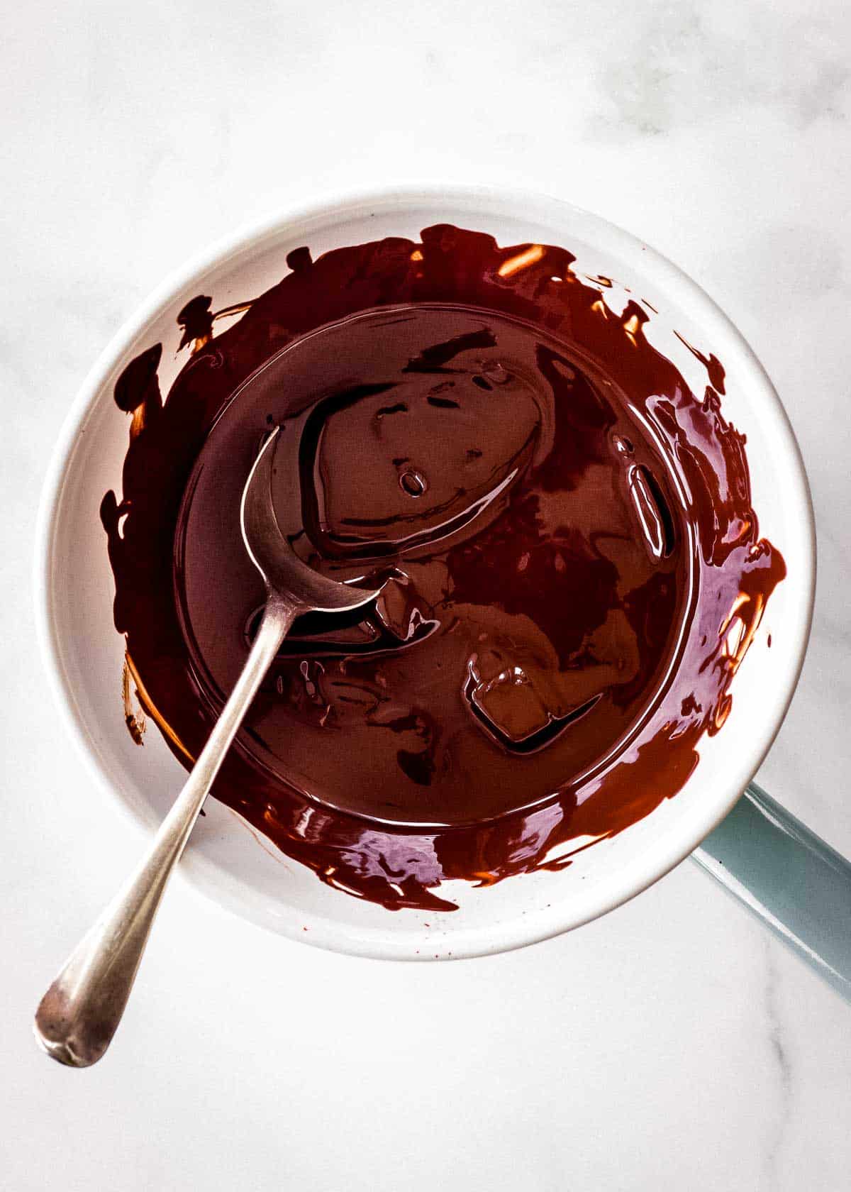 A small bowl over a saucepan is filled with melted dark chocolate.