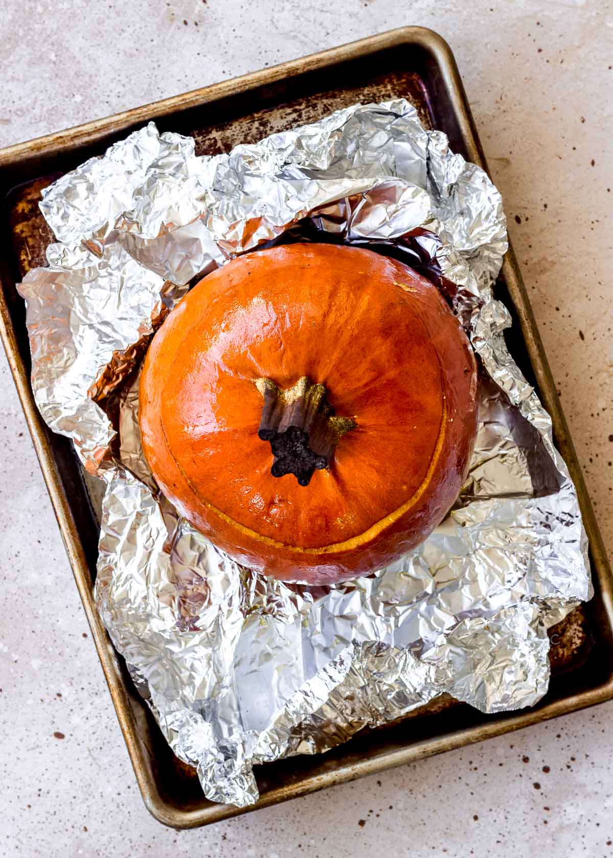 Whole roast pumpkin sits on baking sheet with tin foil removed.