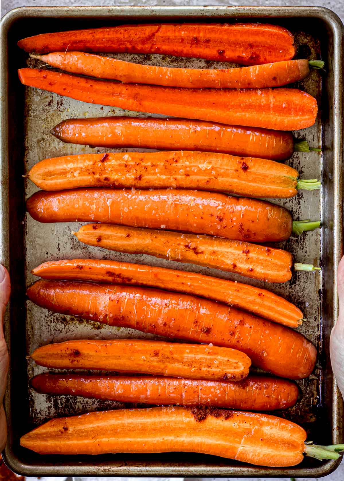 Uncooked carrots sliced in half on a baking sheet, brushed with oil, maple syrup, salt and cayenne pepper.