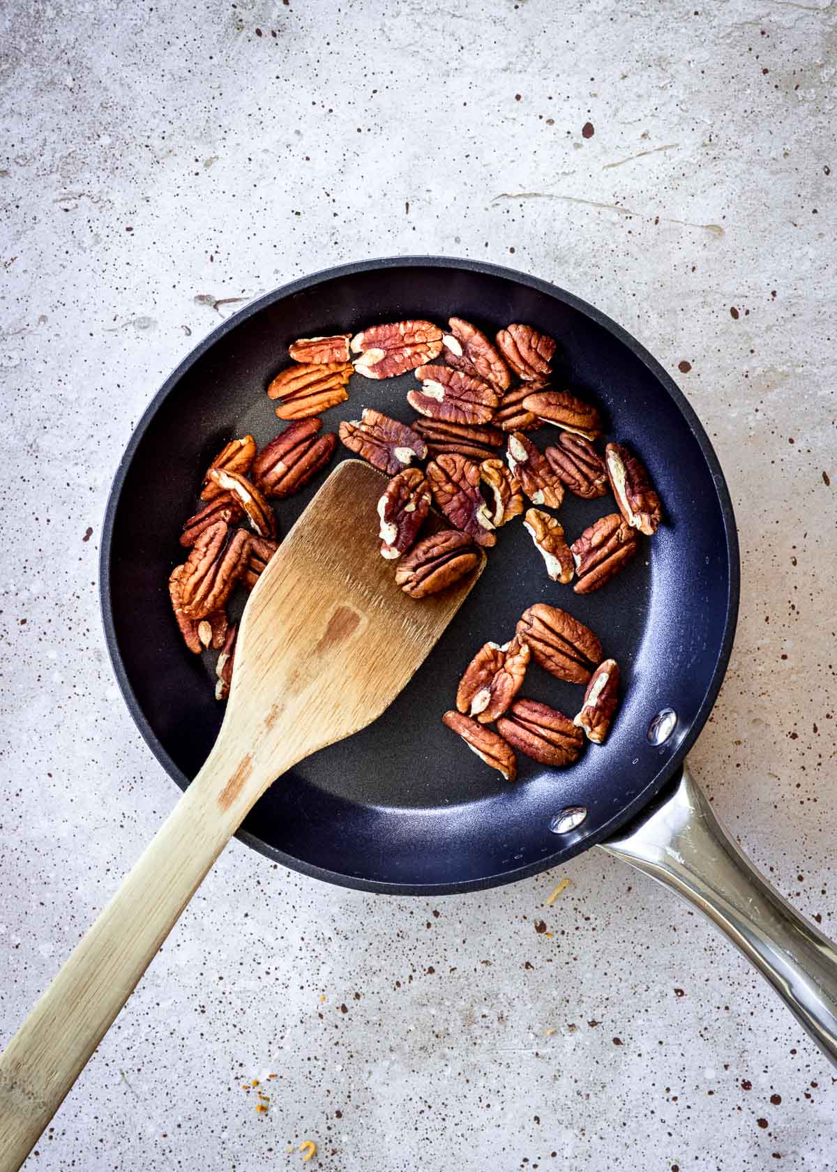Pecans being toasted in shallow small skillet, with wooden spatula.