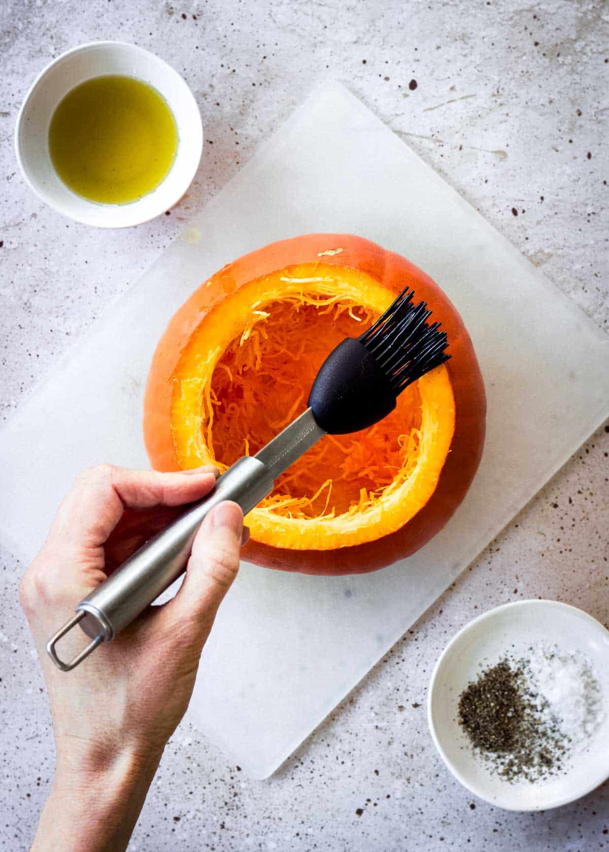 Woman's hand brushing hollowed pumpkin with olive oil.