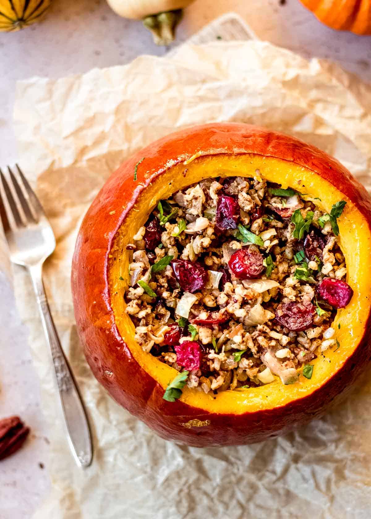 Vegan stuffed pumpkin with rice, pecans and cranberry filling sits on parchment paper, with small decorated squash and fork in background.