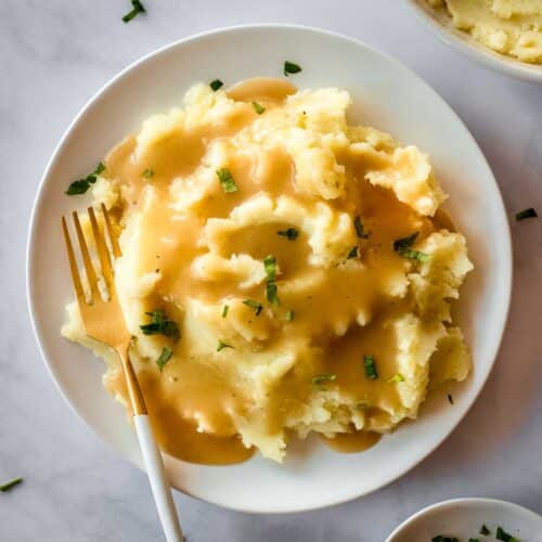 White plate of mashed potatoes and easy vegan gravy, decorated with parsley leaves.
