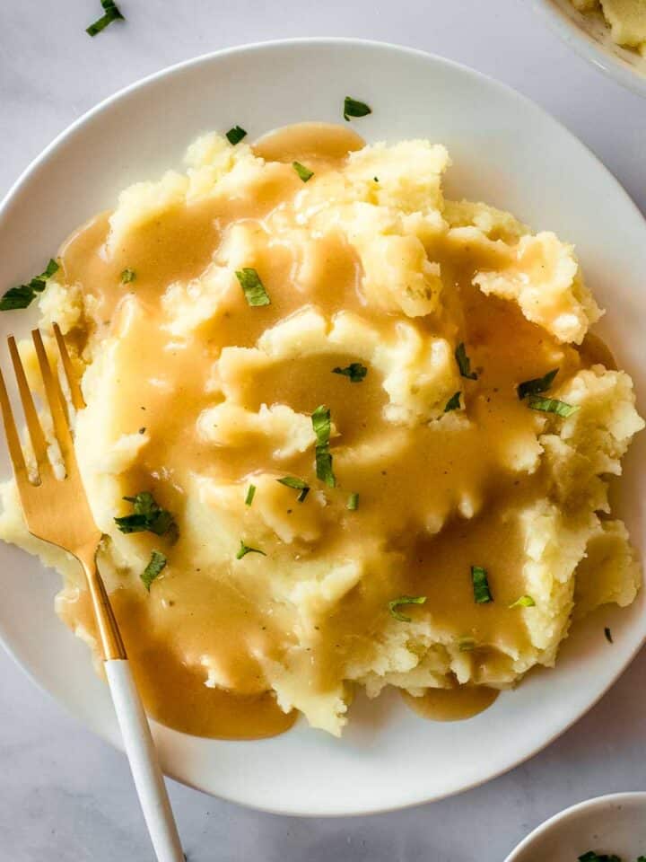 White plate of mashed potatoes and easy vegan gravy, decorated with parsley leaves.