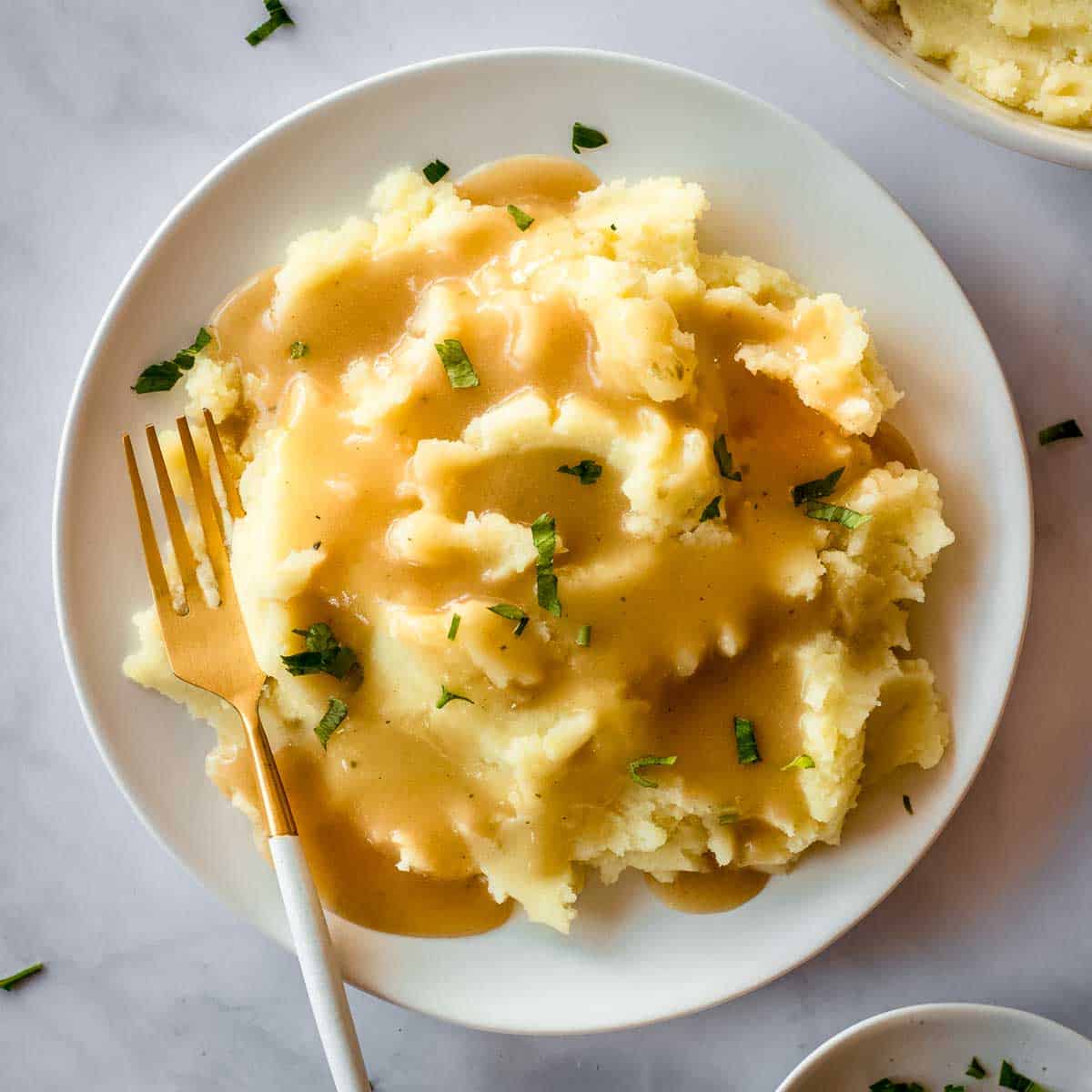 White plate of mashed potatoes and vegan gravy with a gold fork.