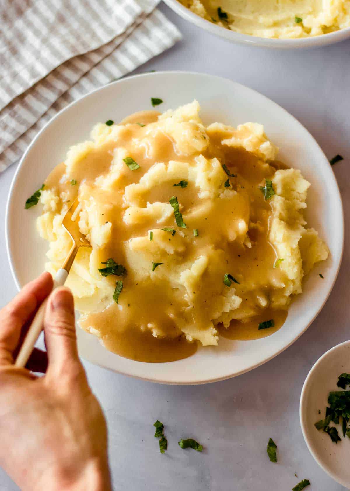A woman's hand takes a forkful of mashed potatoes with easy vegan gravy from a white plate.