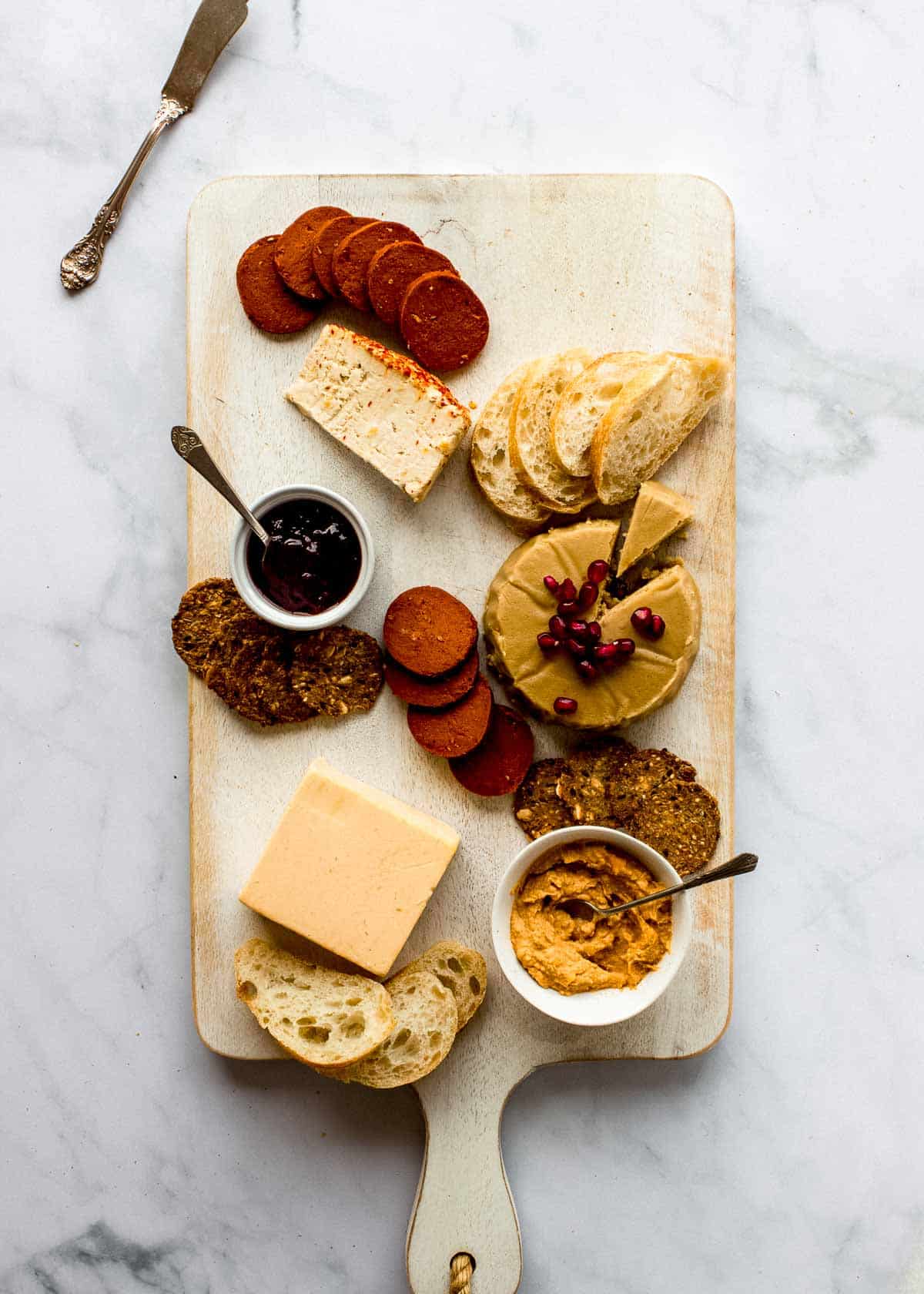 Half-made vegan charcuterie board, featuring plant-based pepperoni, vegan cheeses, crackers and bread.