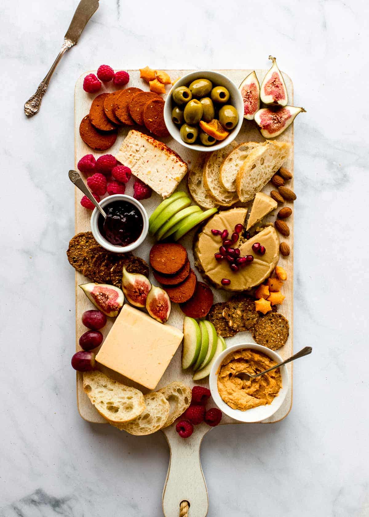 A rectangular vegan cheese board, featuring vegan cheese, plant-based meats, fruits, bread and crackers.