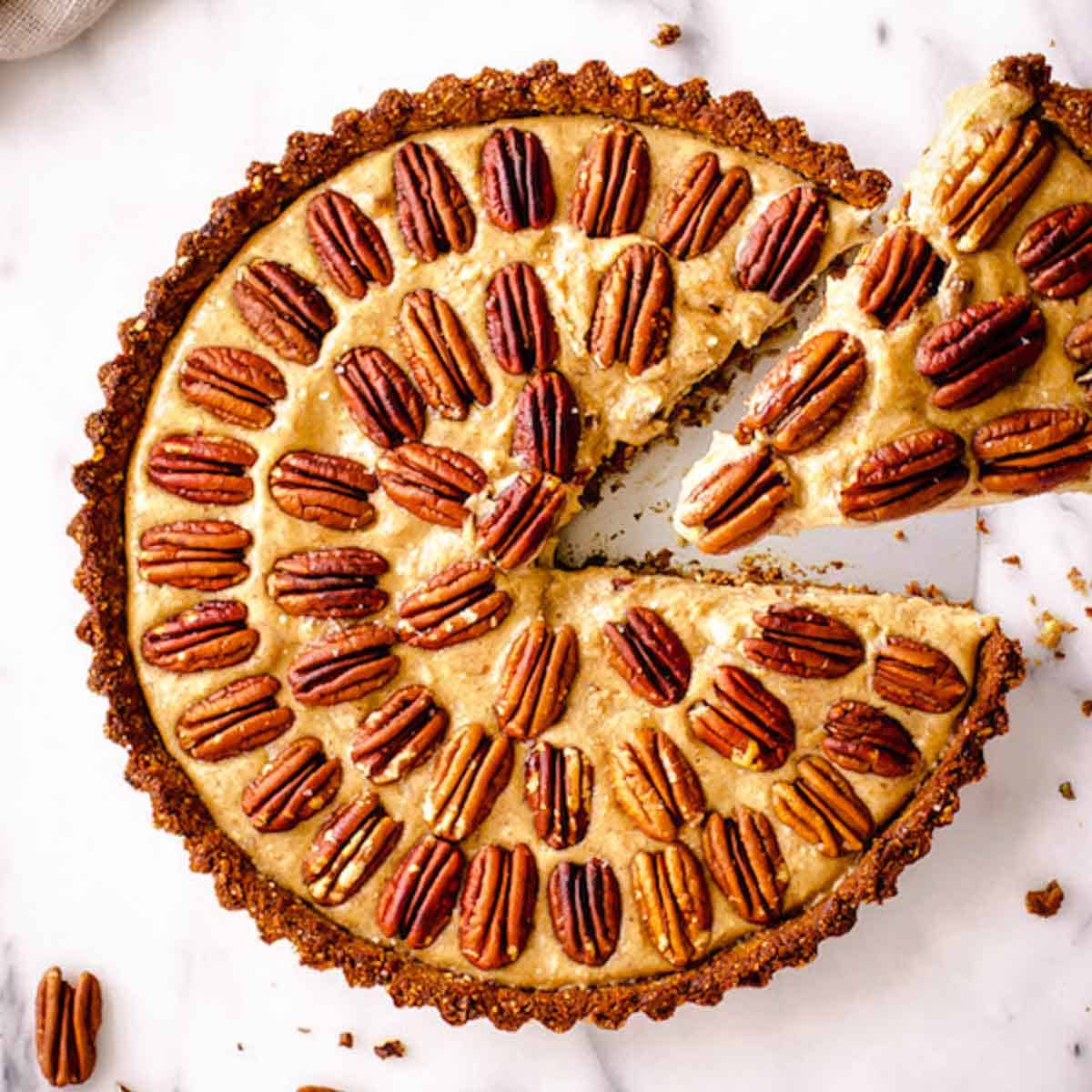 Overhead view of vegan pecan pie with concentric circles of pecans. A slice is being taken.
