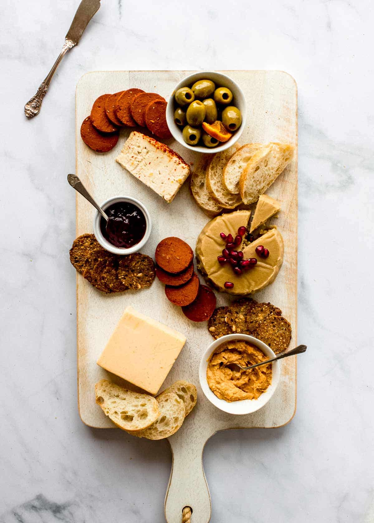 Three different types of cheeses, bread, crackers, olives, jam and pepperoni on a vegan platter.