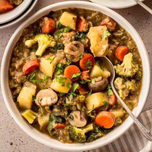 White bowl of easy vegetable stew with carrots, mushrooms, broccoli and lentils. A spoon is in the bowl.