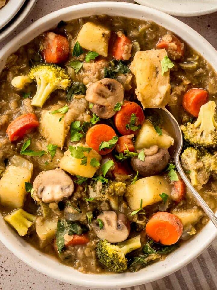 White bowl of easy vegetable stew with carrots, mushrooms, broccoli and lentils. A spoon is in the bowl.