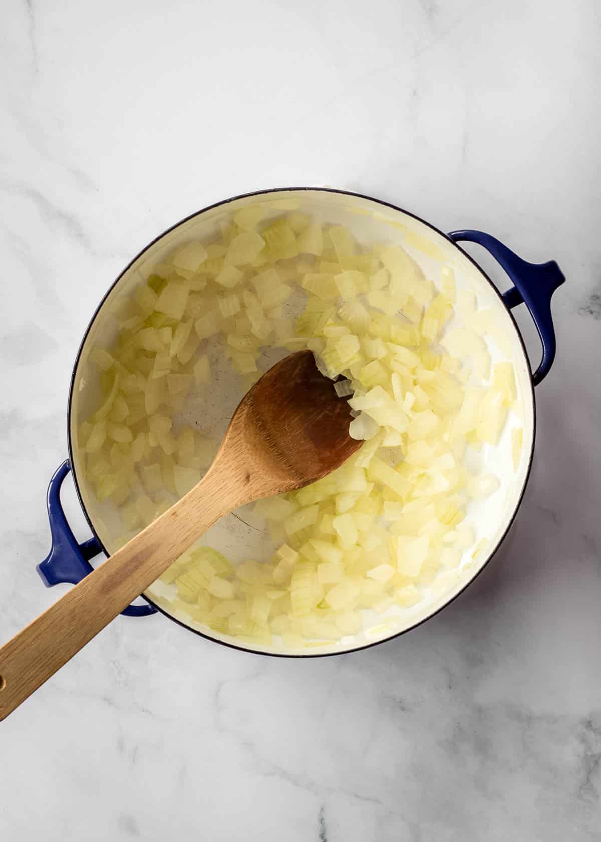 Onion being sautéed in a large dark blue pot with a wooden spoon.