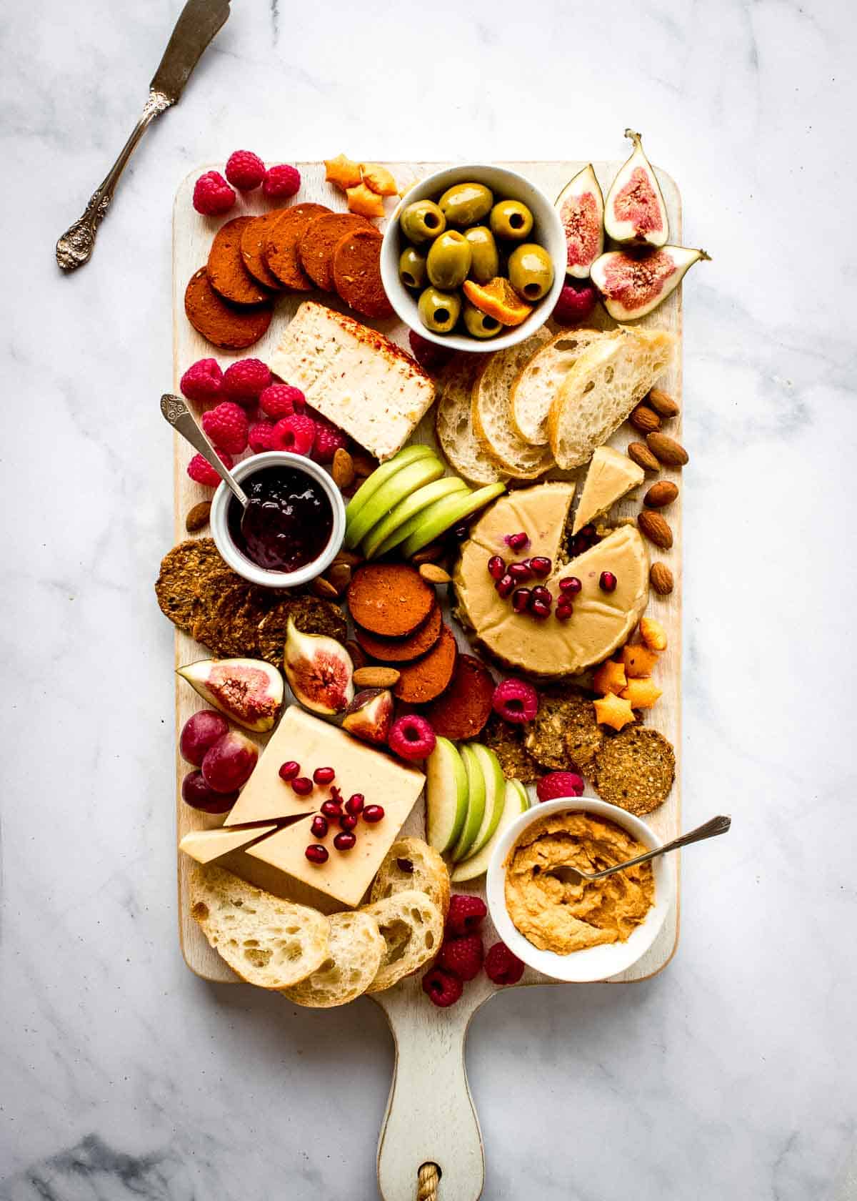 A rectangular vegetarian charcuterie board, featuring vegan cheese, plant-based meats, fruits, bread and crackers.