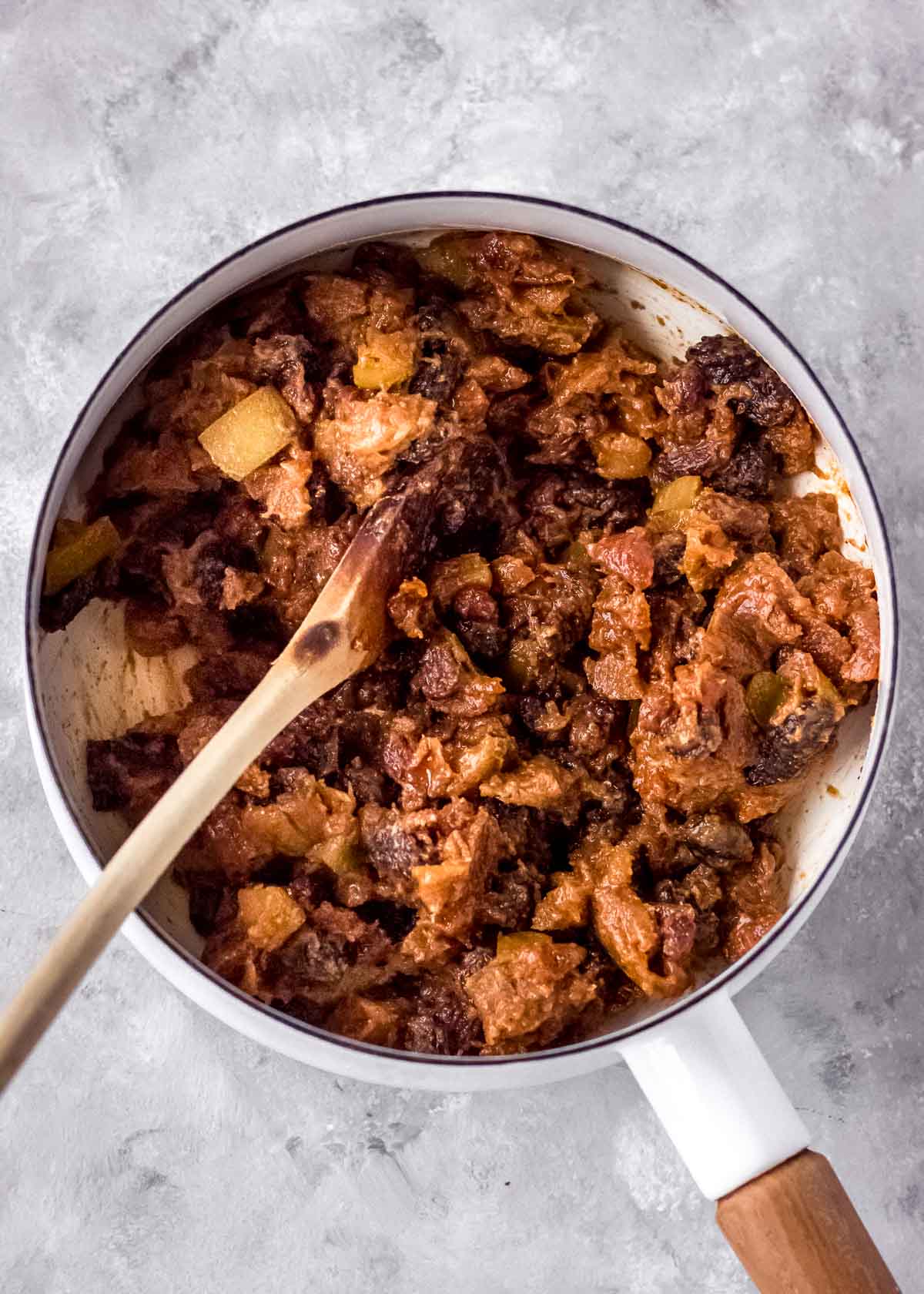 Sweet vegan mincemeat cooking in a white saucepan with a wooden spoon.