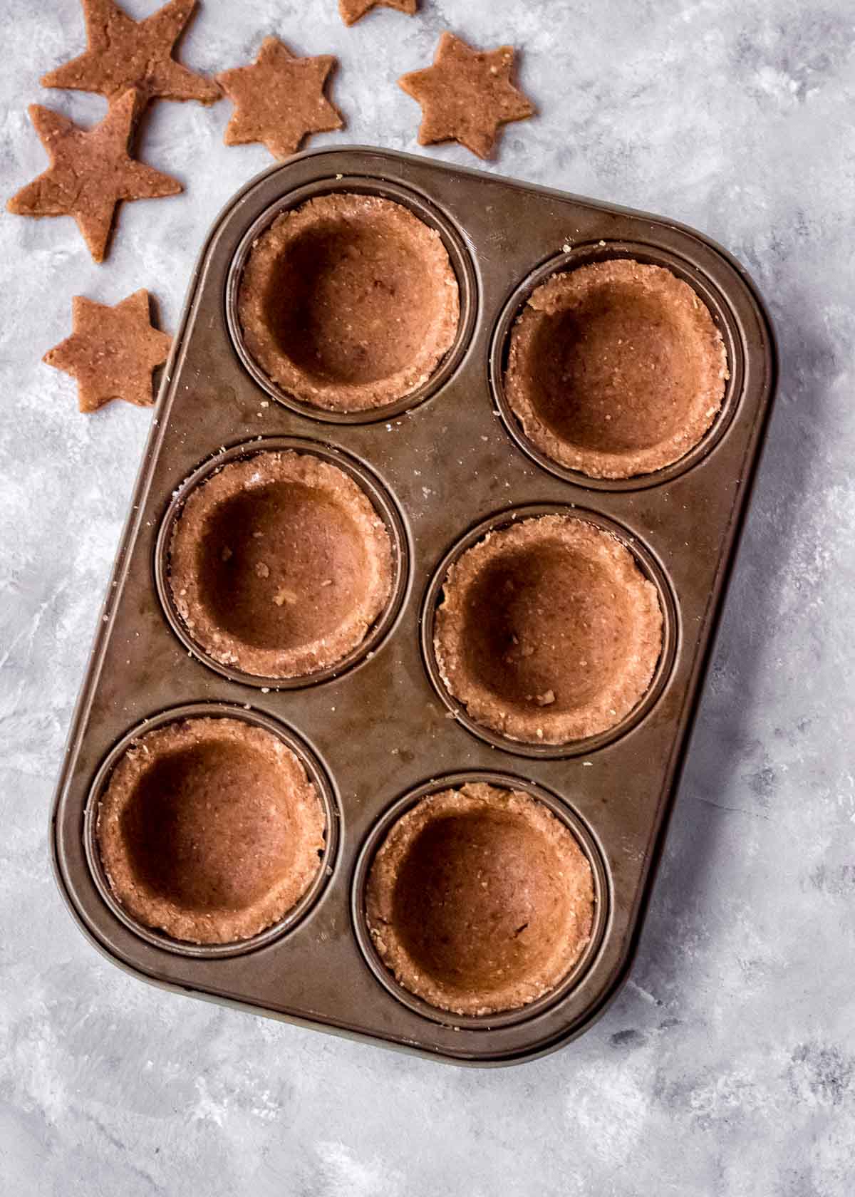 Empty vegan mince pie shells sit in muffin tins, with pastry stars nearby.