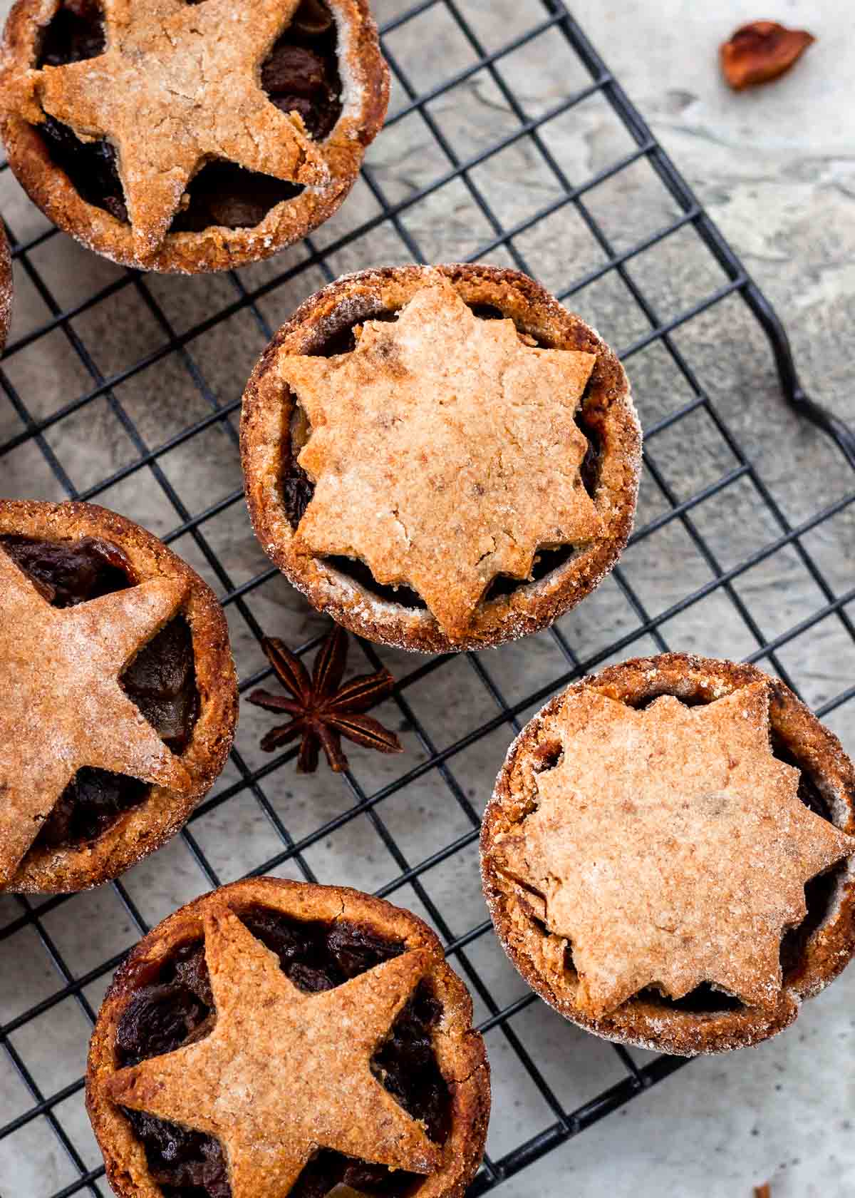 Festive mince pies with pastry stars sit cooling on rack.
