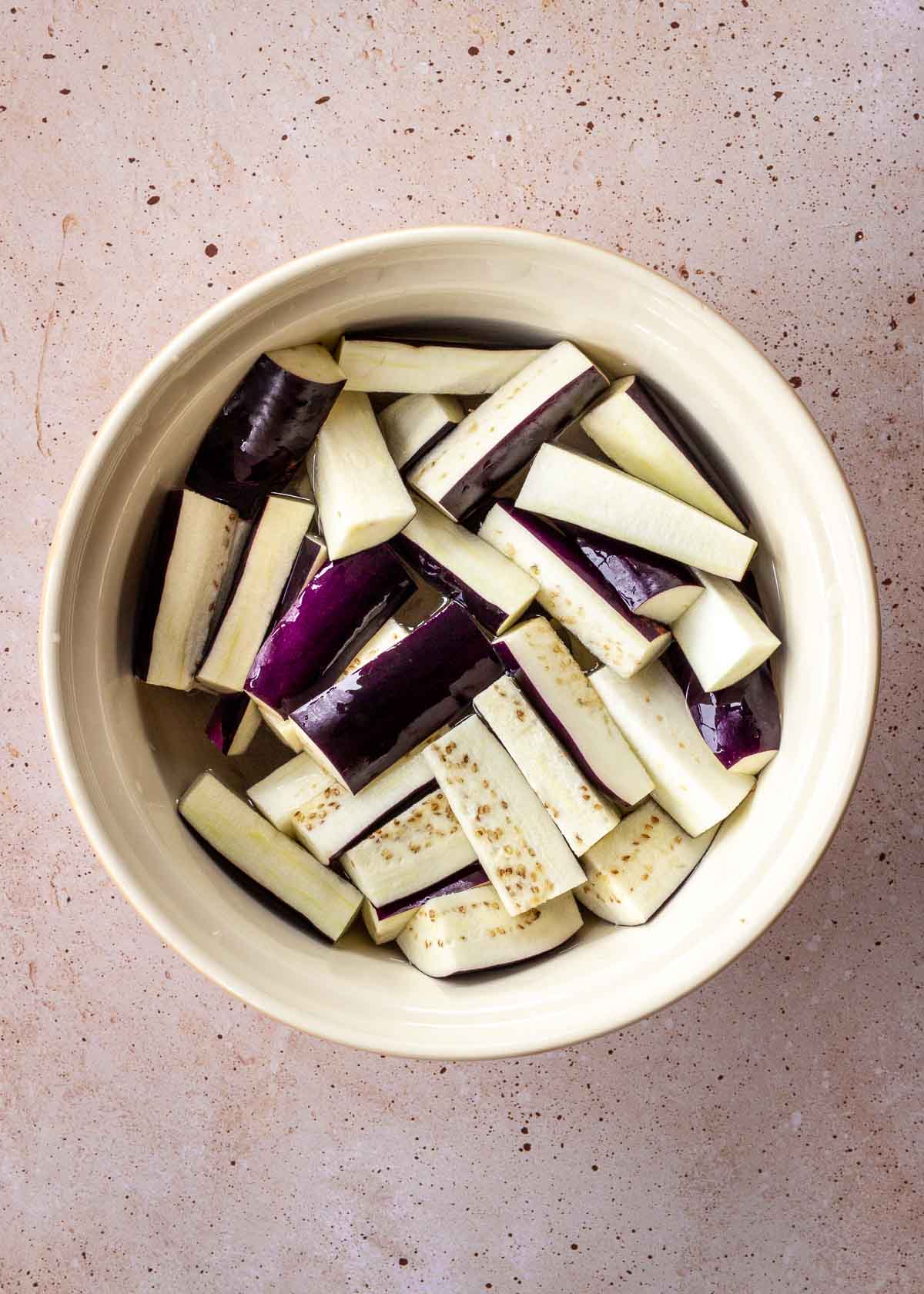 Large white bowl of eggplant slices in salt water.