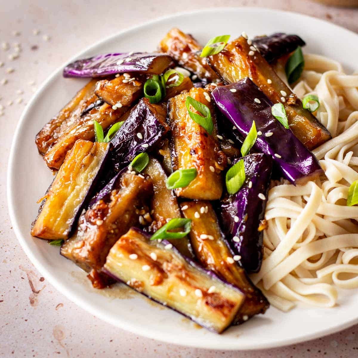 White plate of eggplant stir fry with garlic sauce, decorated with green onions and sesame.