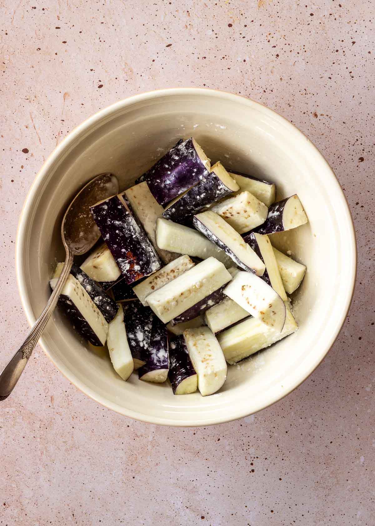 A large white bowl of eggplant slices being mixed with cornstarch.