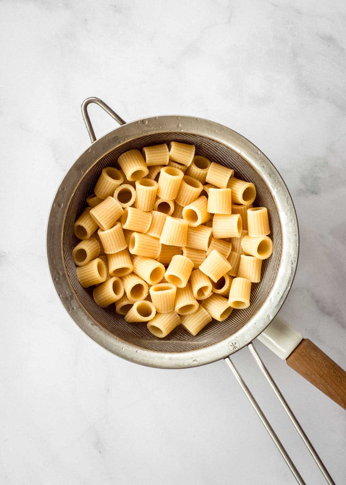 A sieve full of cooked rigatoni pasta.