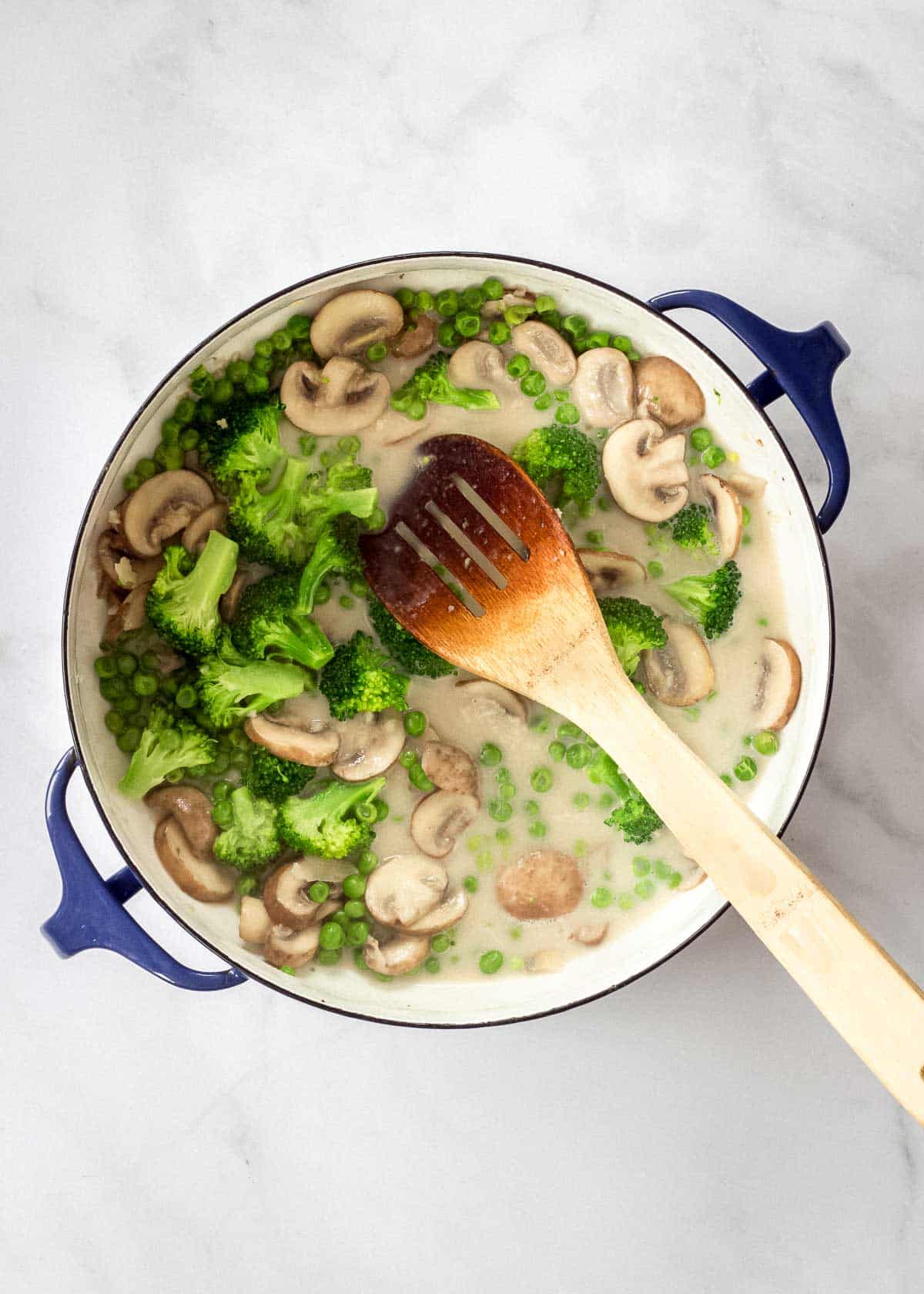Large enamel pot with wooden spoon filled with mushroom broccoli pasta sauce.