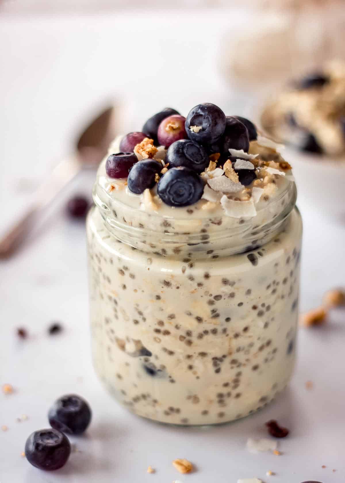 Glass jar of blueberry overnight oatmeal, topped with blueberries and granola.
