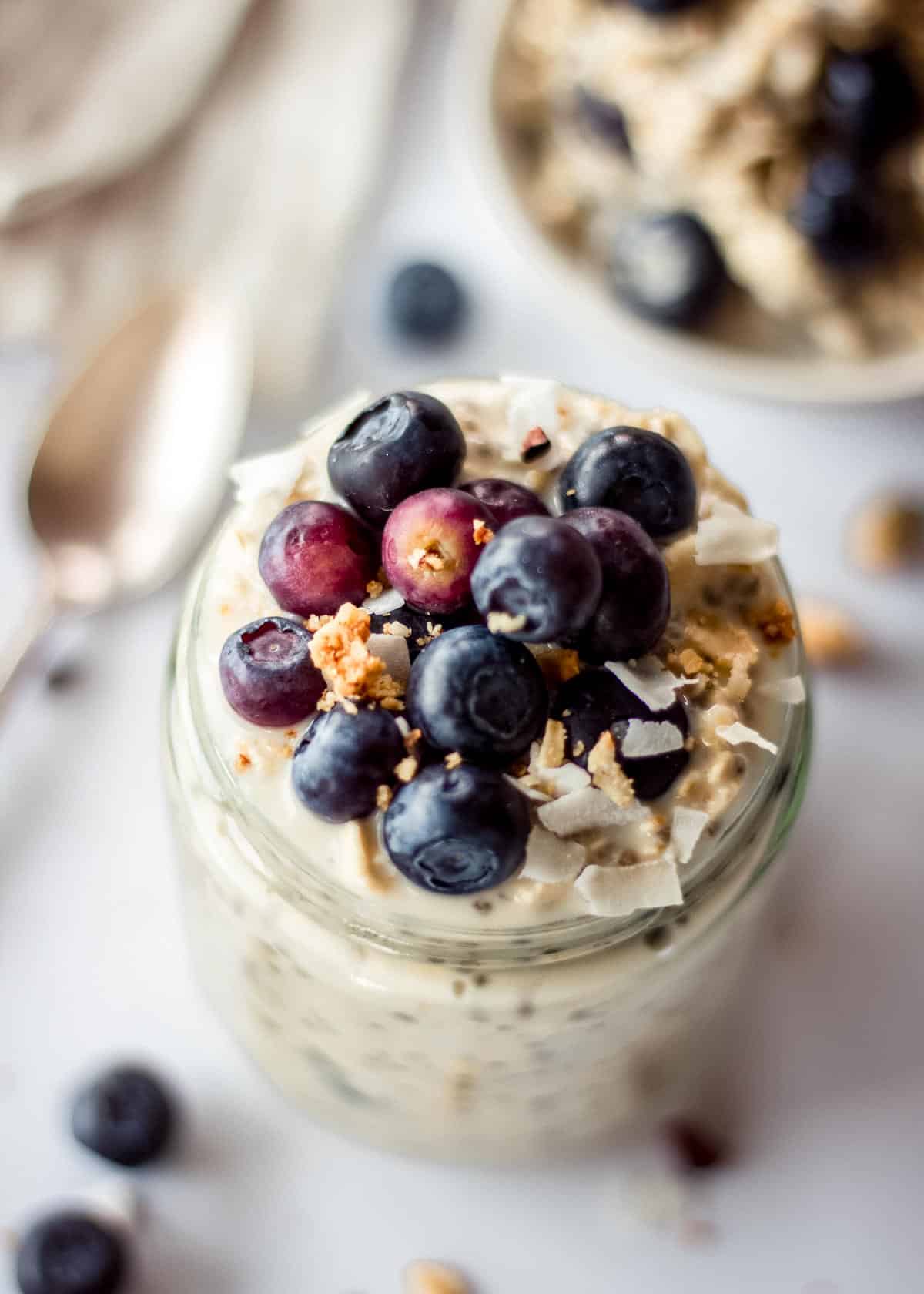 Glass jar of blueberry overnight oats, topped with blueberries, coconut and granola.
