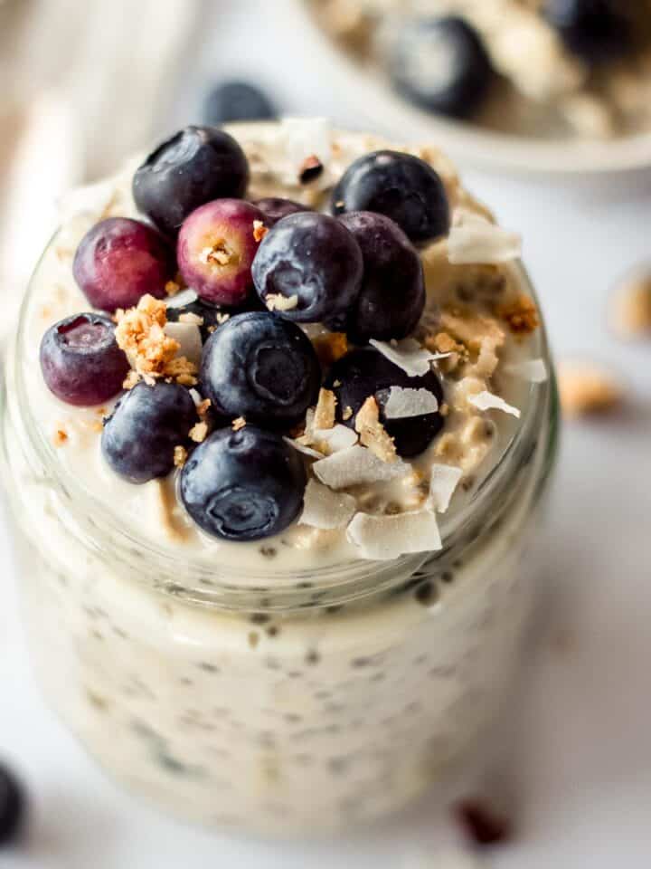 Mason jar of blueberry overnight oats, topped with blueberries, coconut and granola.