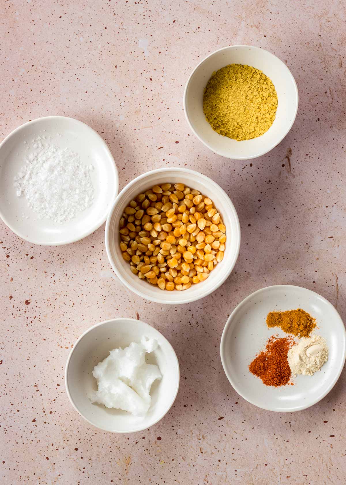 Ingredients to make vegan popcorn, including corn kernels, nutritional yeast, coconut oil, smoked paprika and salt.