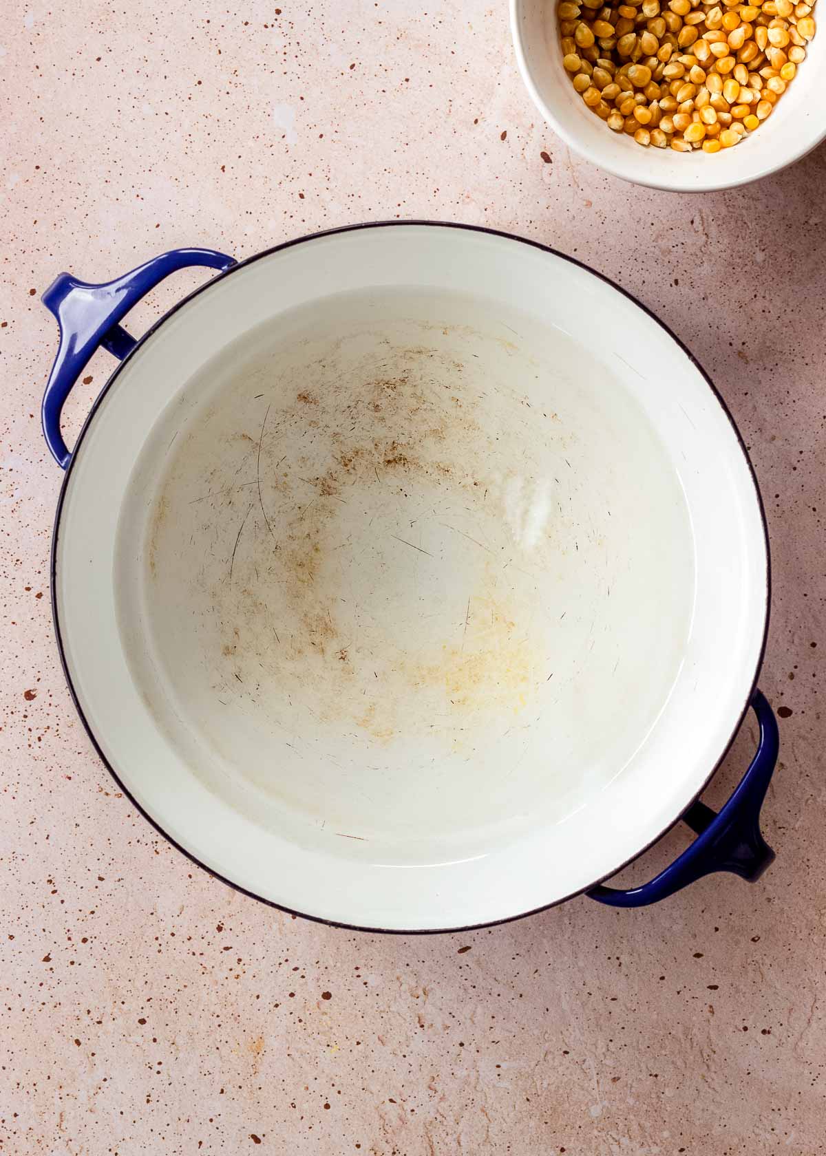 A large pot containing melted hot coconut oil. A small bowl of corn kernels sits nearby.