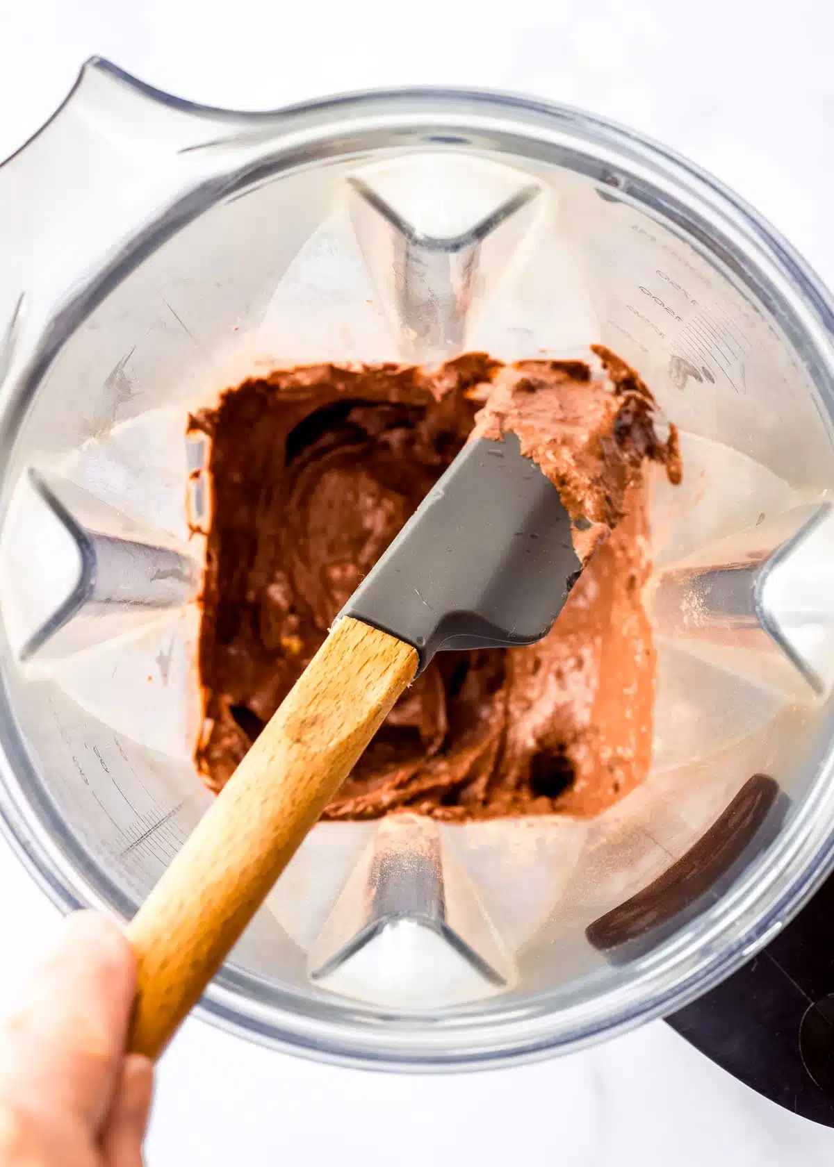A spatula scraping down sides of blender jug filled with avocado chocolate mousse.