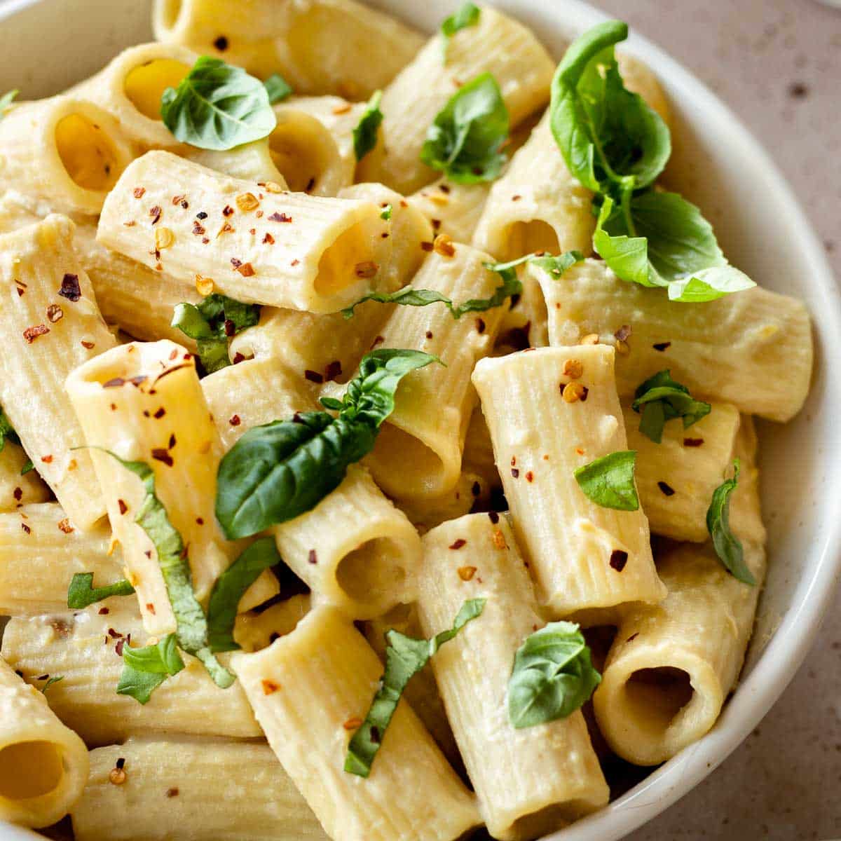 White bowl of tahini pasta decorated with basil leaves.