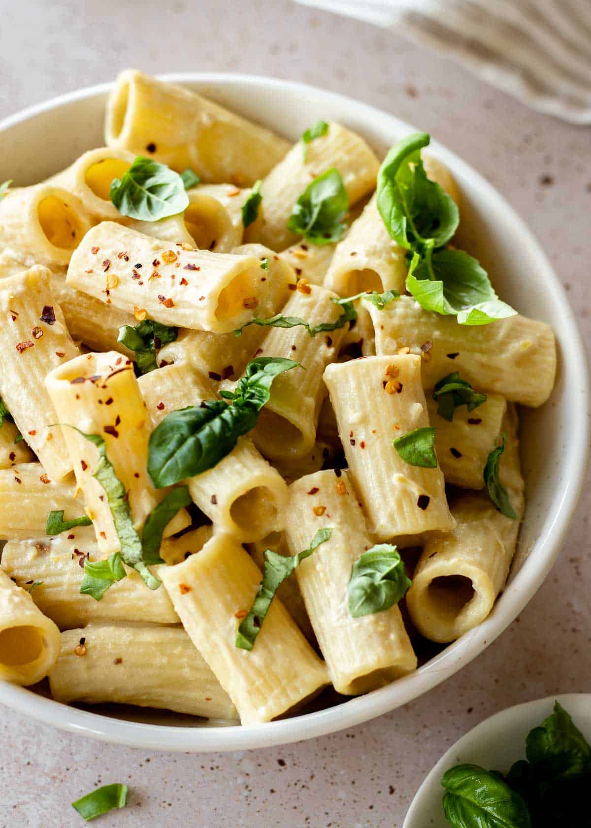 White bowl of tahini pasta decorated with basil and chili flakes.