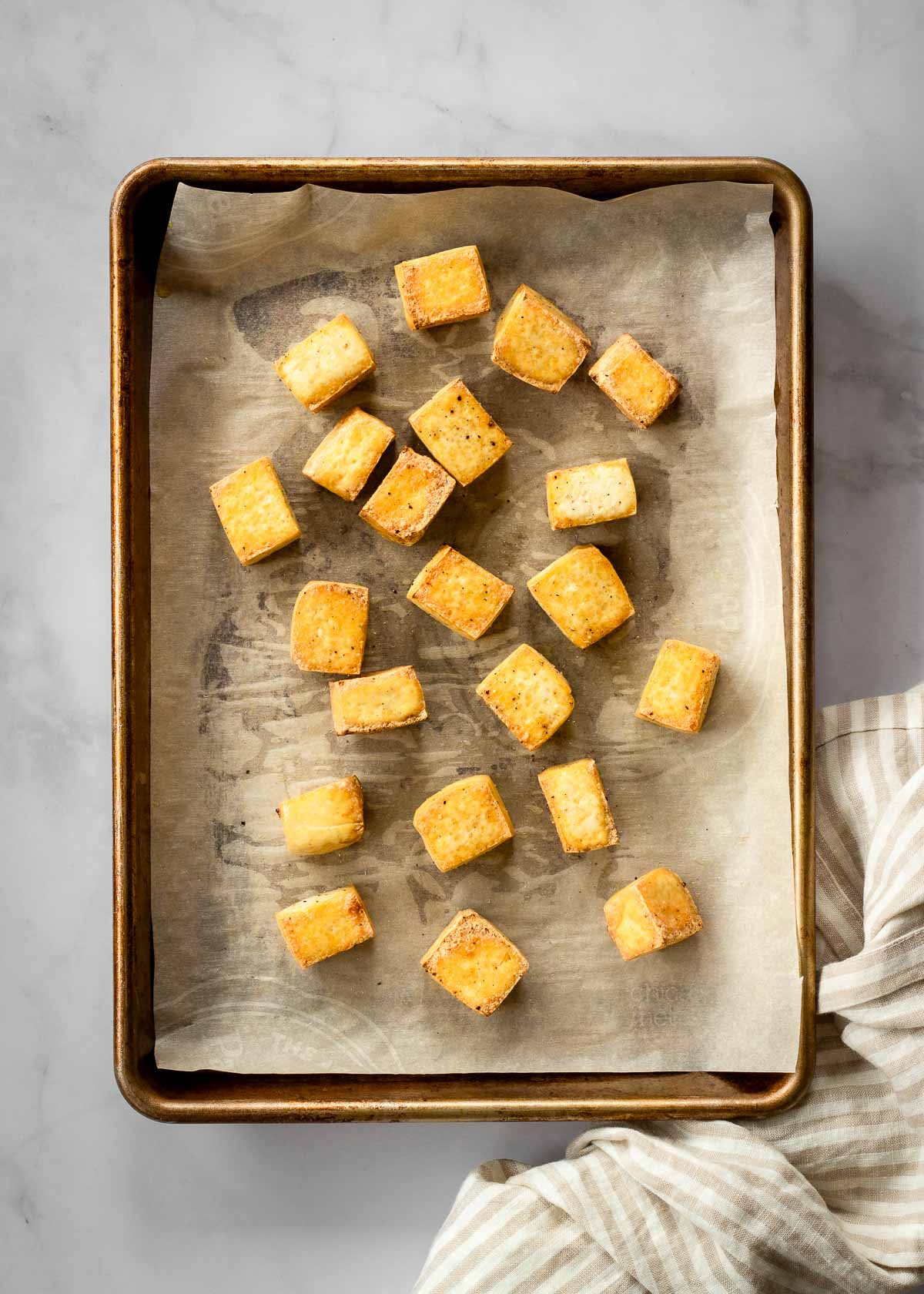 Golden broiled tofu sits on a parchment-lined baking sheet.