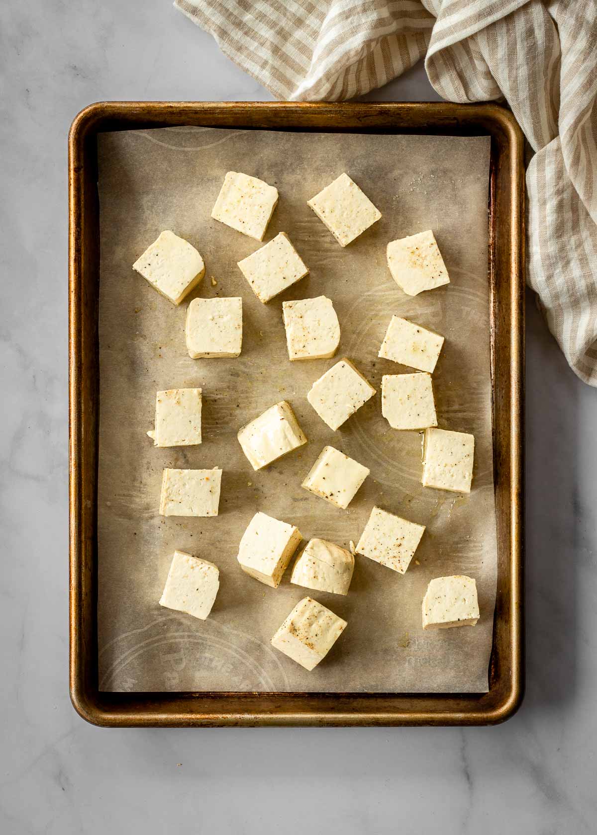 Uncooked tofu sits on a parchment-lined baking sheet.